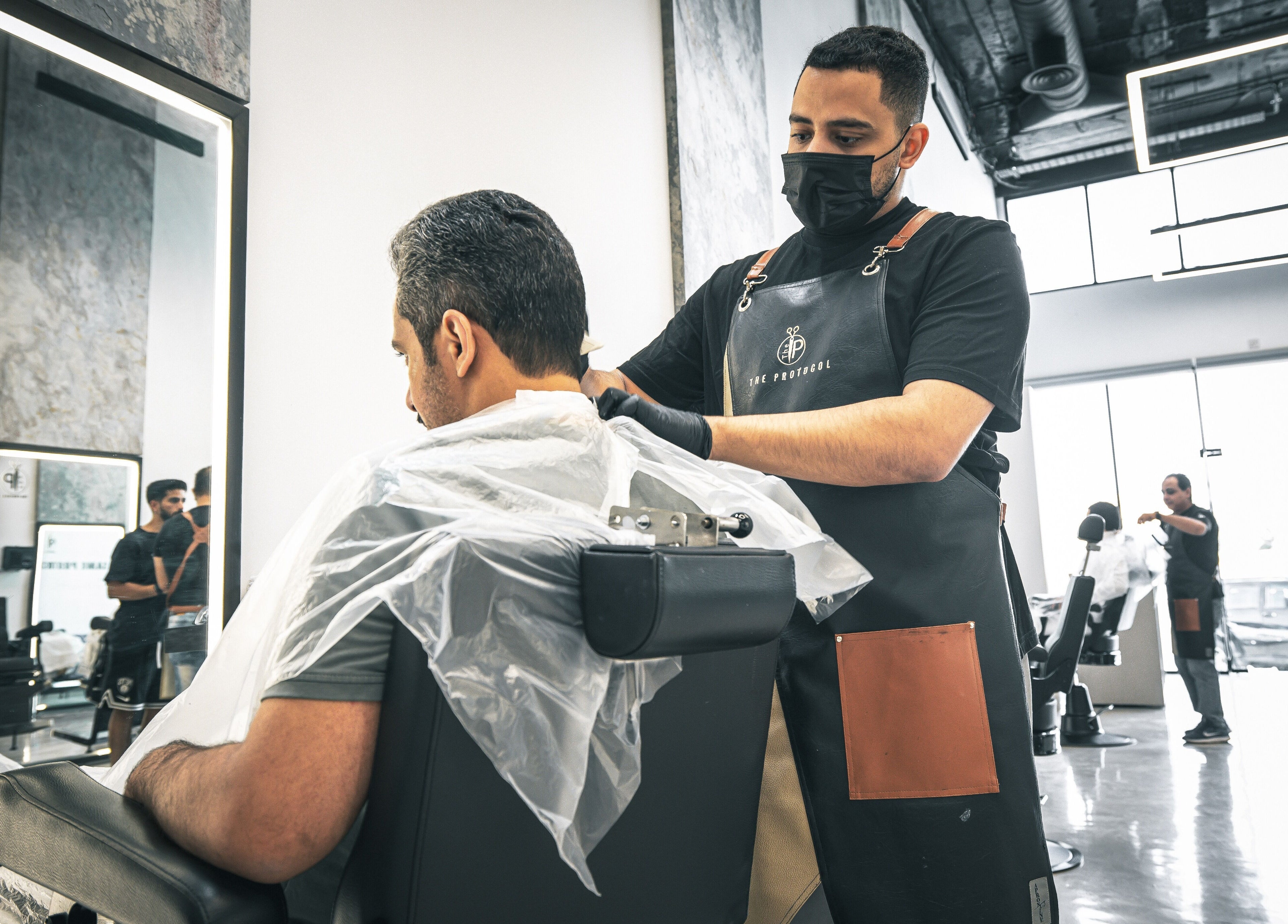 A skilled barber at The Protocol Barbershop in Riyadh, Riyadh Province, SA, expertly trims a client's hair.