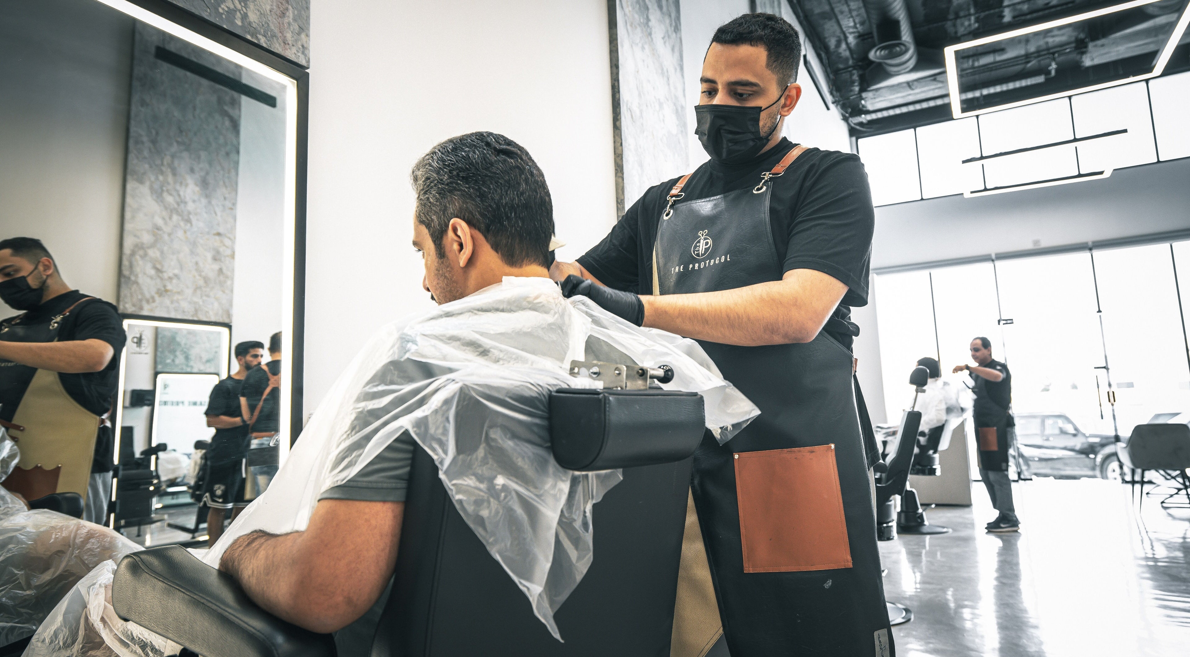 A skilled barber at The Protocol Barbershop in Riyadh, Riyadh Province, SA, expertly trims a client's hair.