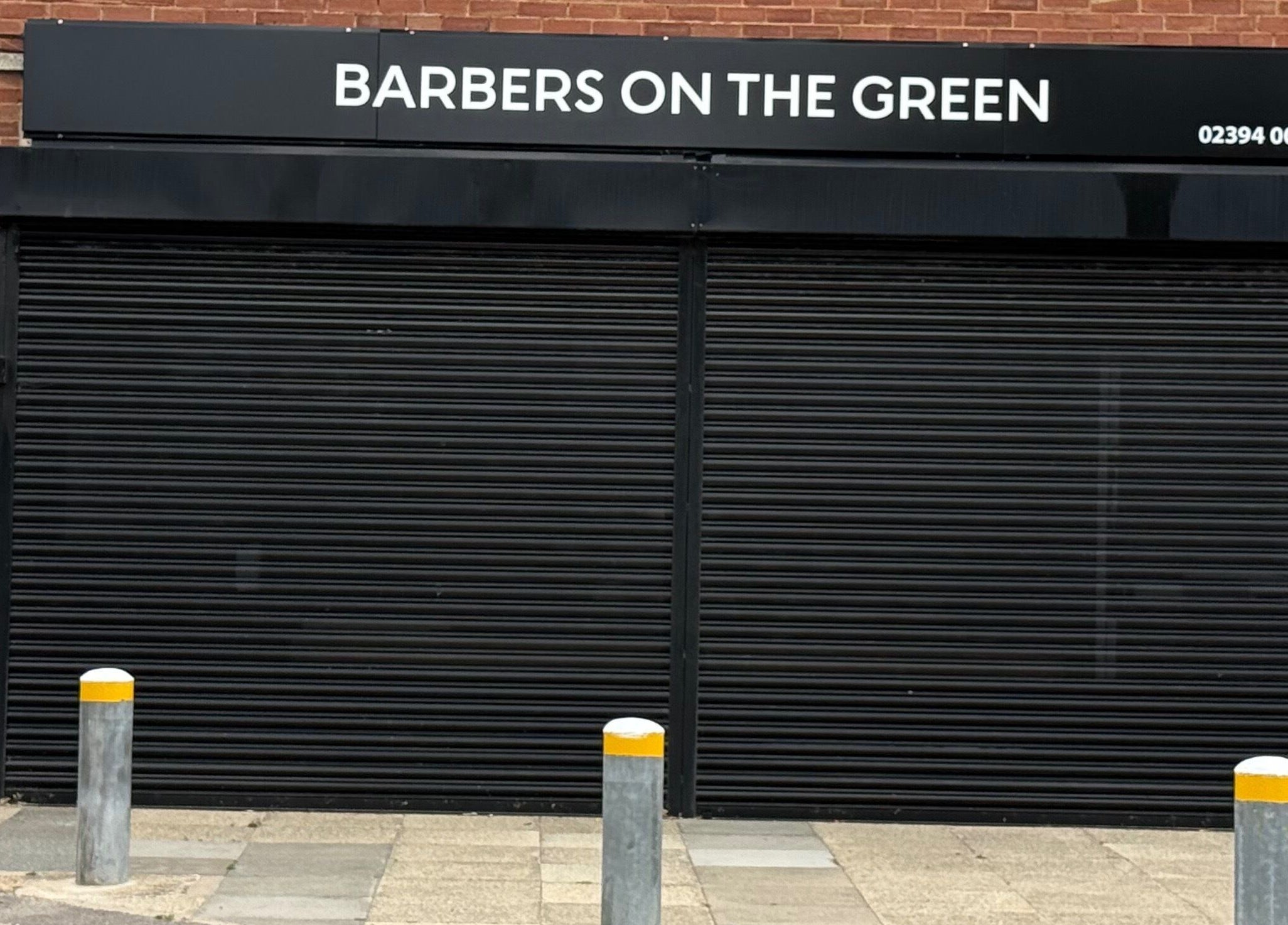Barbers On The Green storefront with closed shutters in Havant, England, GB.