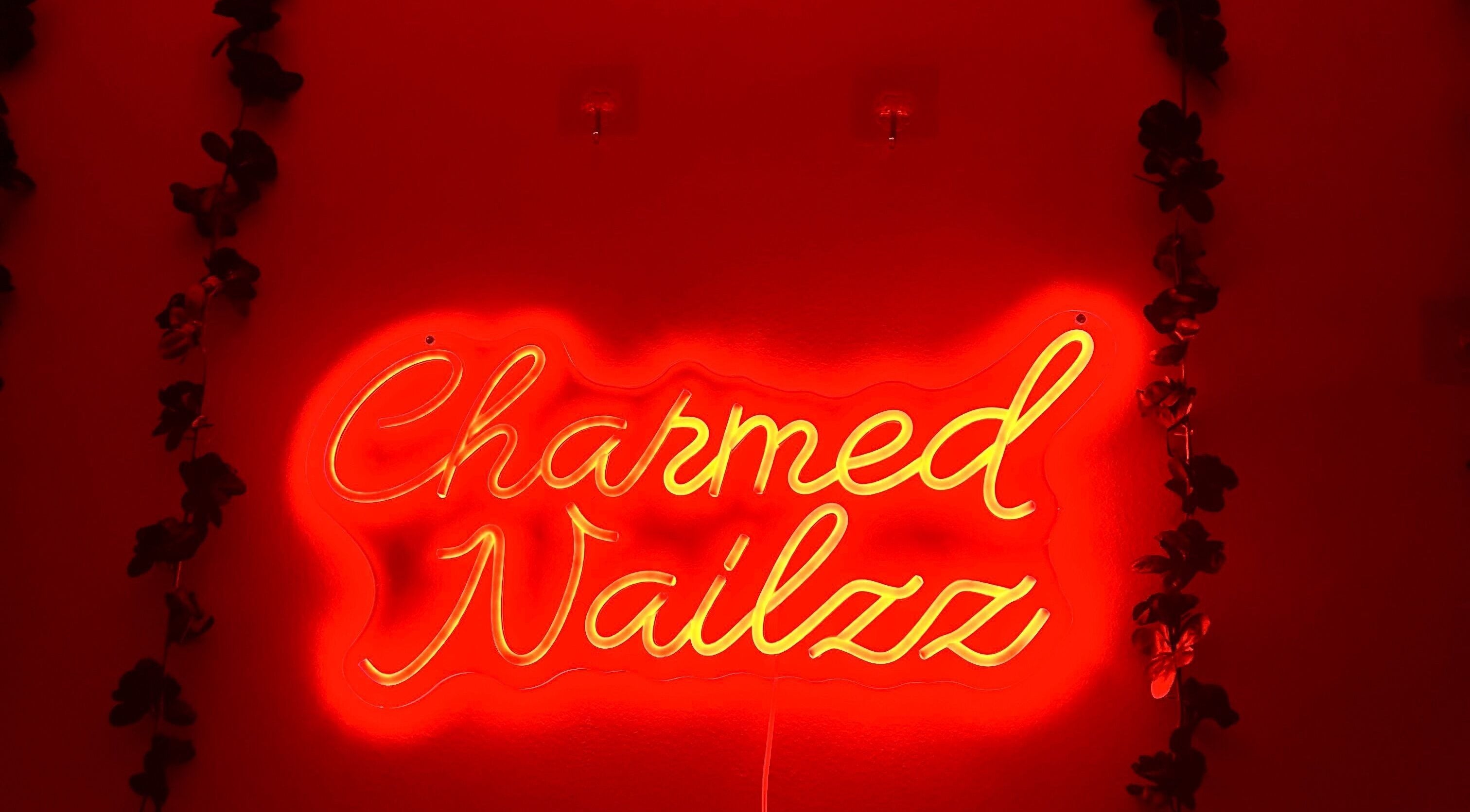 Neon sign at Charmed Nailzz in Red Deer, Alberta, CA burns brightly against a decorative backdrop.
