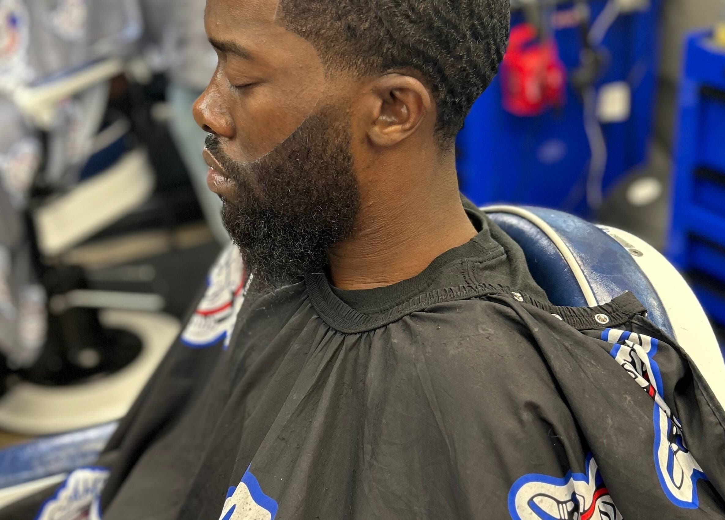 Man getting a precise haircut at Den Of Sauce, Lathrup, Michigan, US. Blue and black barber chair.