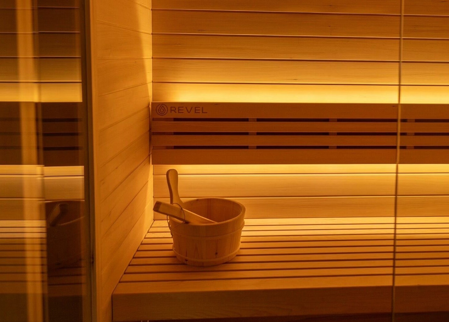 Elegant sauna room at Aura Sweat, Thirroul, New South Wales, AU, illuminated warmly with wooden seating and bucket.