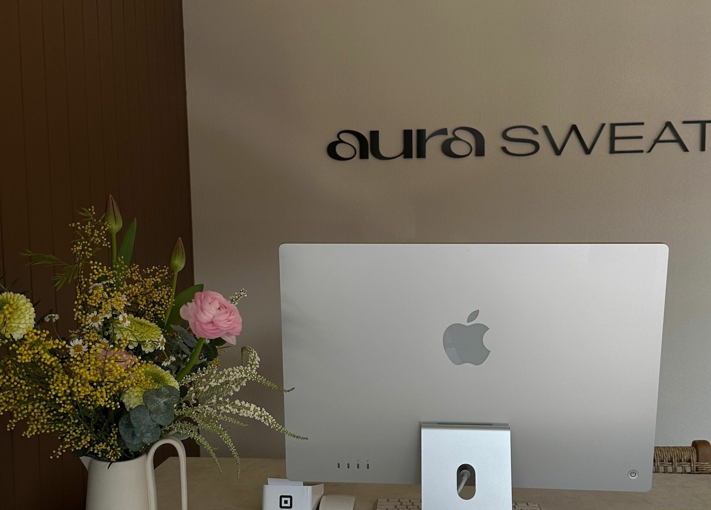 Reception desk at Aura Sweat, Thirroul, New South Wales, AU, featuring a computer and a floral arrangement.