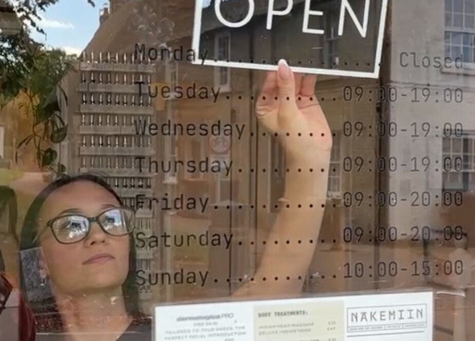 Person adjusting open sign at Näkemiin, Harrold, England, GB, showcasing operating hours.