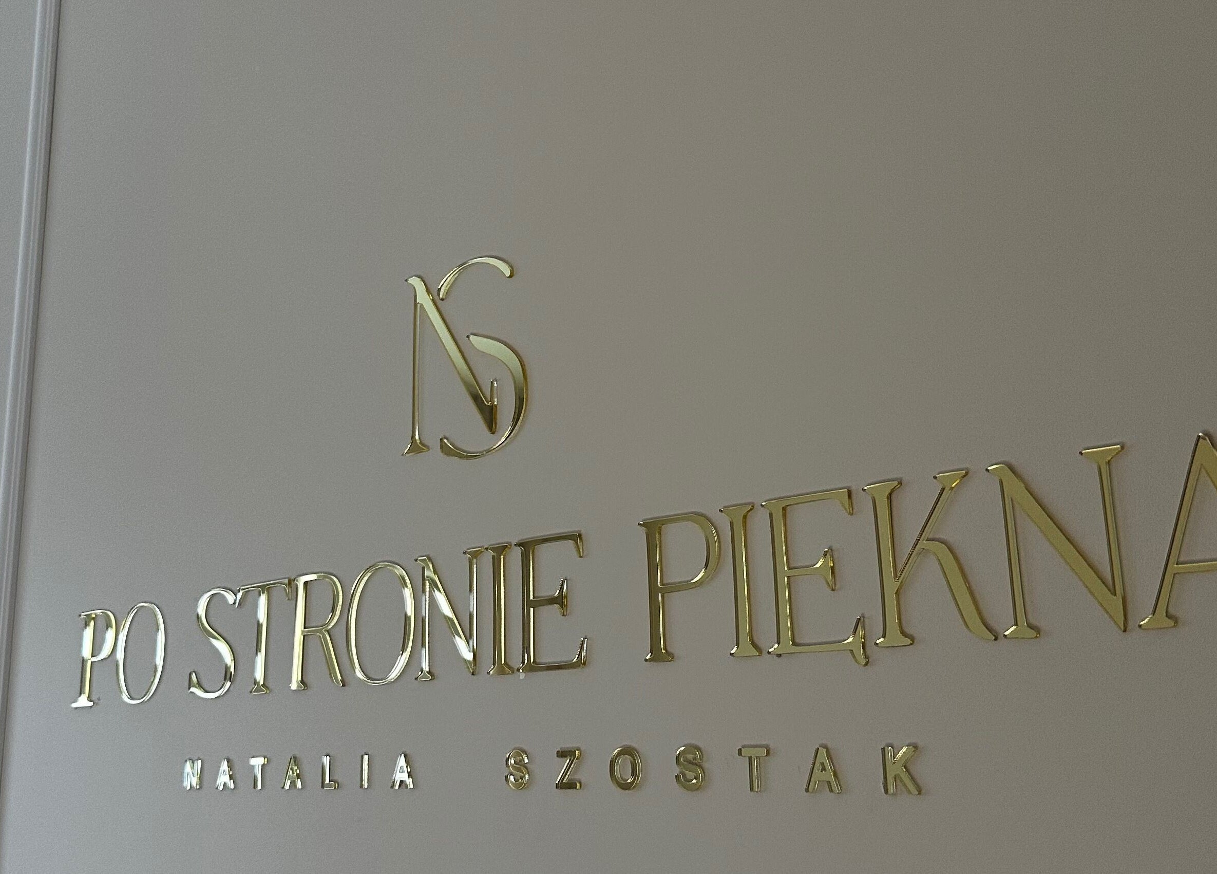 Złote logo Po stronie piękna na ścianie w Olsztynie, Województwo Warmińsko-mazurskie, PL.