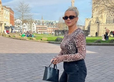 Stylish woman walks near Get Sprayed, Exeter, England, GB with historic architecture in view.