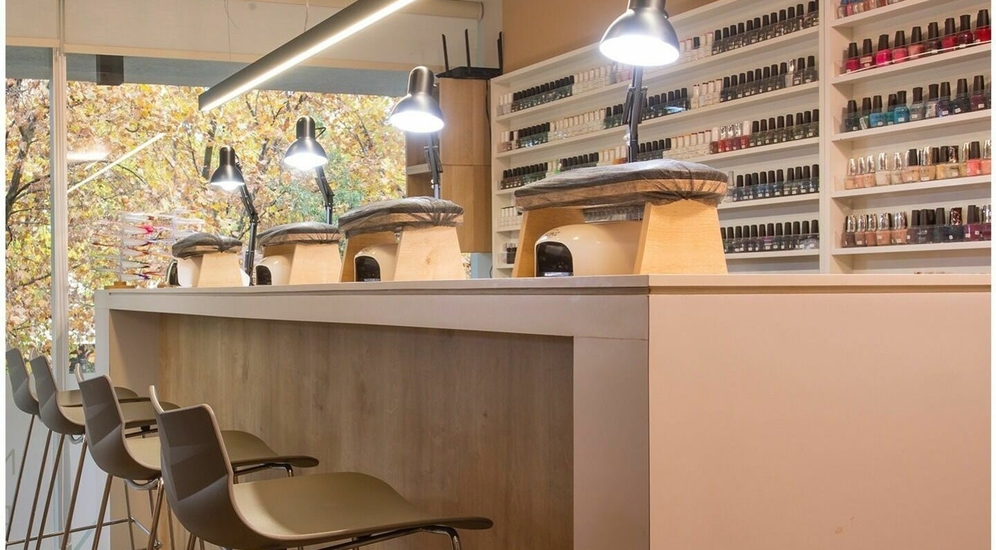 Interior moderno de Nails Bar en Santiago, Región Metropolitana, CL con estantes de esmaltes y sillas elegantes.