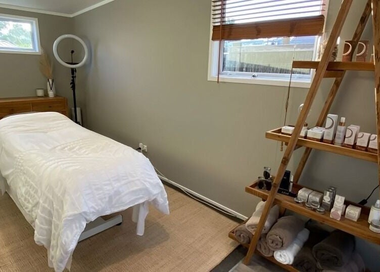 Relaxing treatment room at Tonic Beauté, Auckland, NZ, with cozy bed and wellness products on shelves.