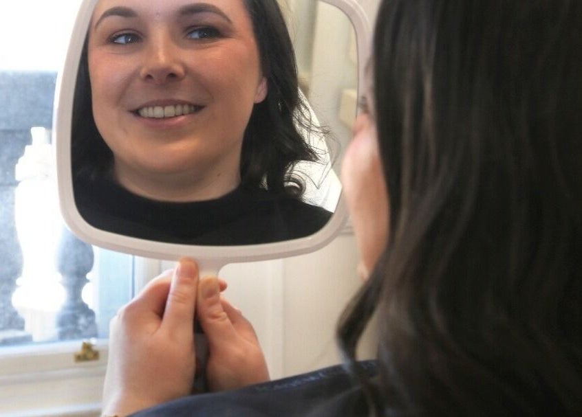 Smiling woman admires her reflection at Stella Medical Aesthetics in Dublin, County Dublin, IE.