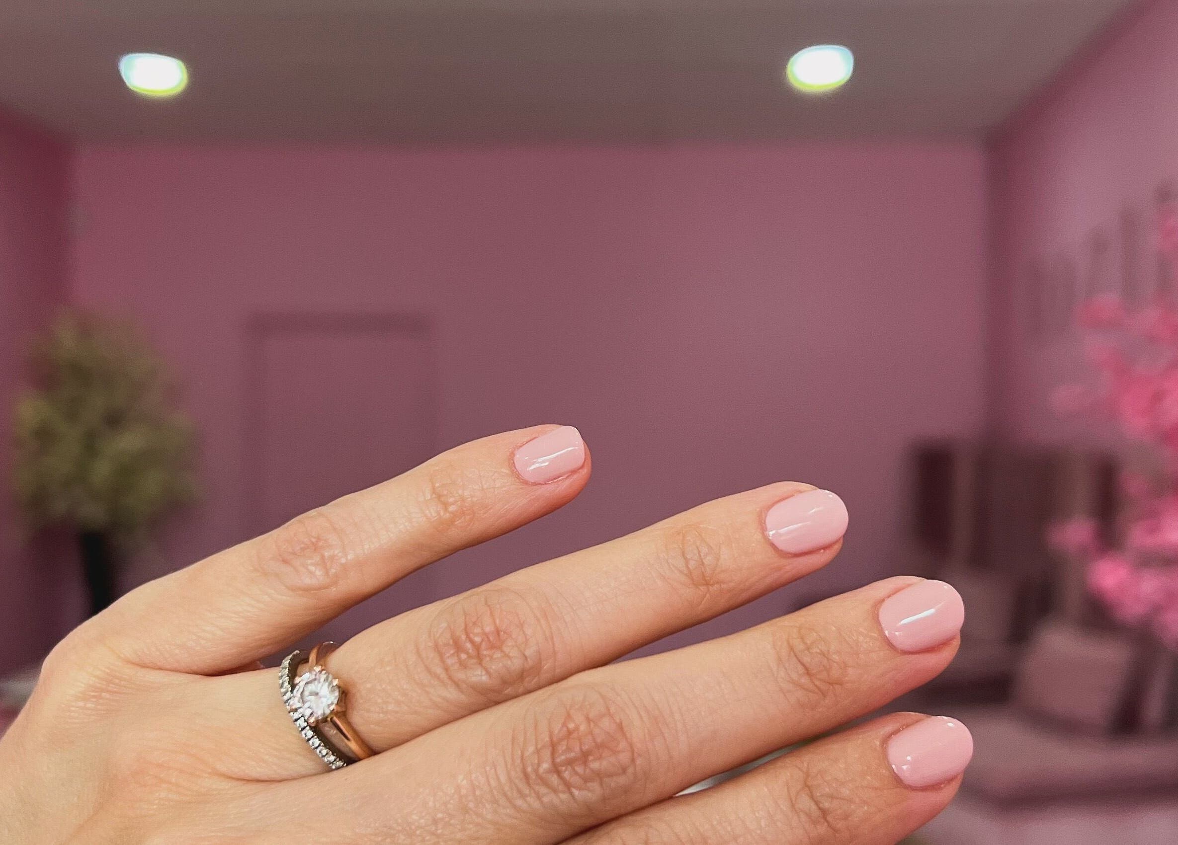 Manicured hand with pink nails at ROZÏÏ JŪ, East London, Eastern Cape, ZA, set against a pink salon backdrop.