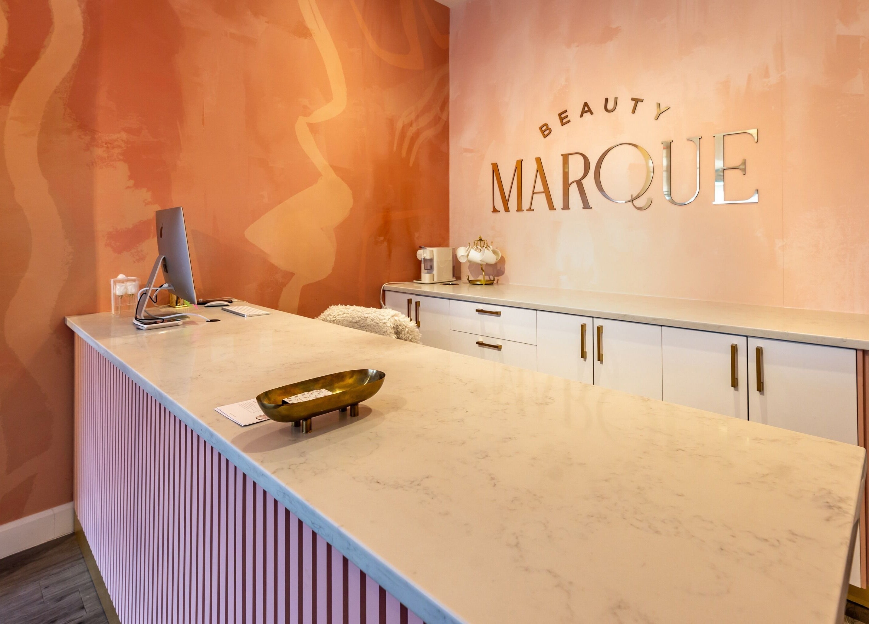 Reception area of Beauty Marque, Pointe-Claire, Québec, CA with stylish pink decor and sleek counter.