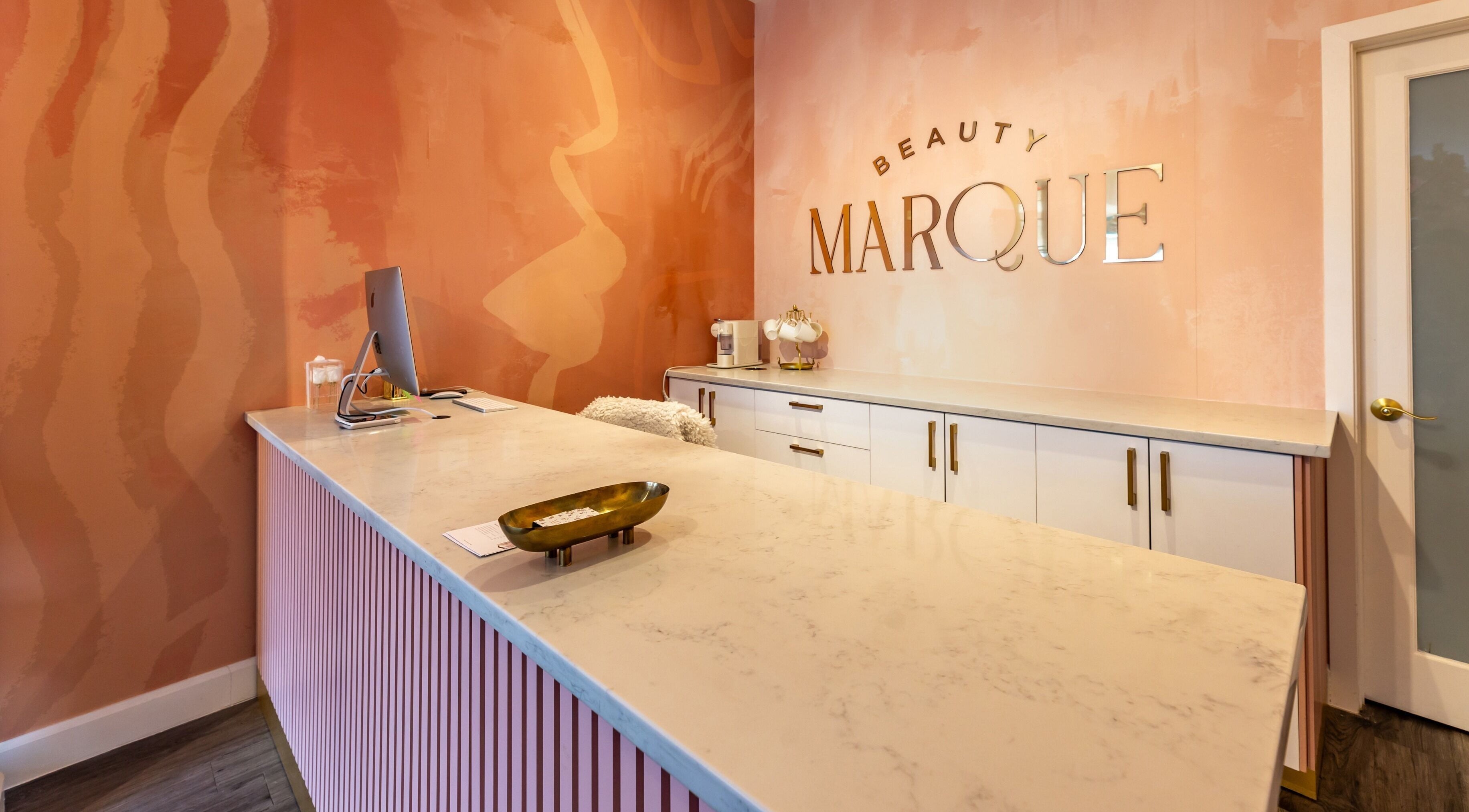 Reception area of Beauty Marque, Pointe-Claire, Québec, CA with stylish pink decor and sleek counter.