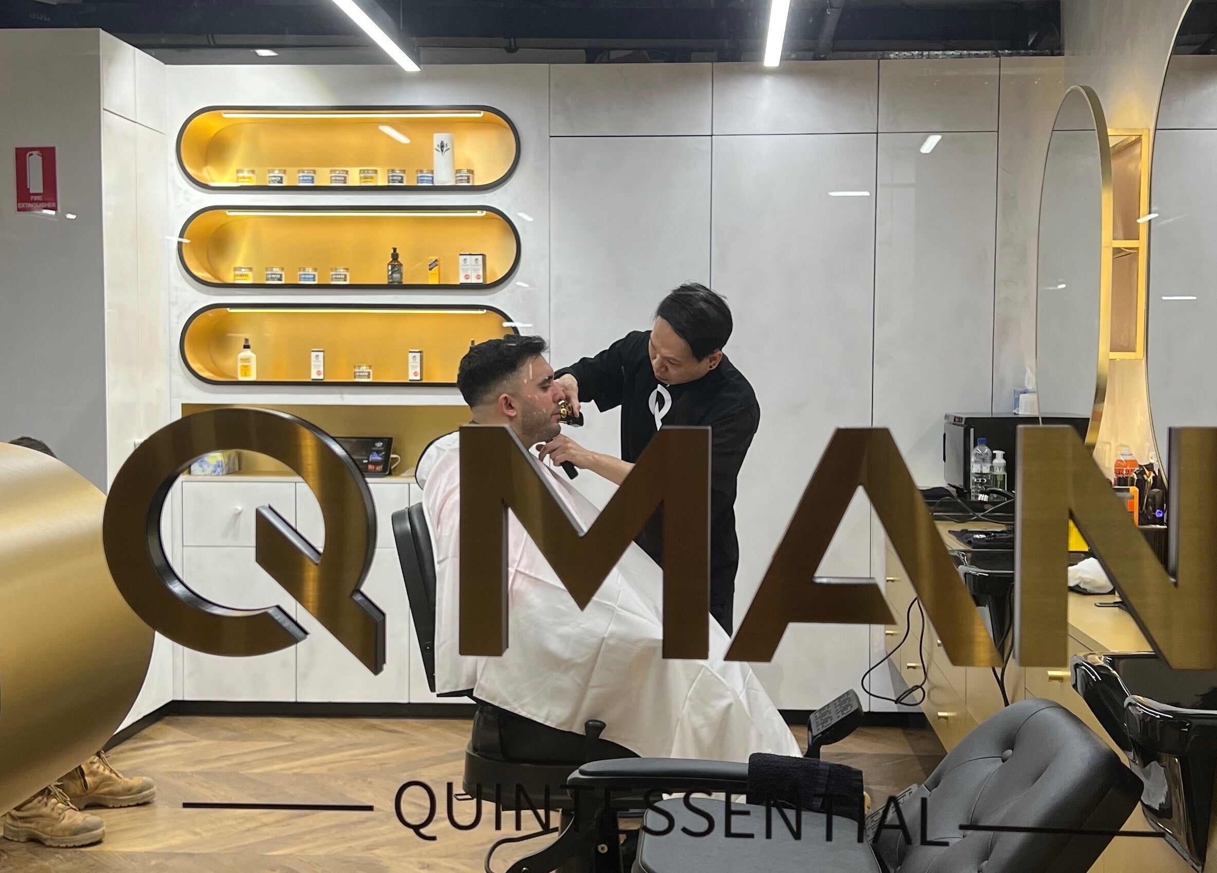 Inside Quintessential Man, Redfern, NSW: A barber trims a client's beard in a stylish modern setting.