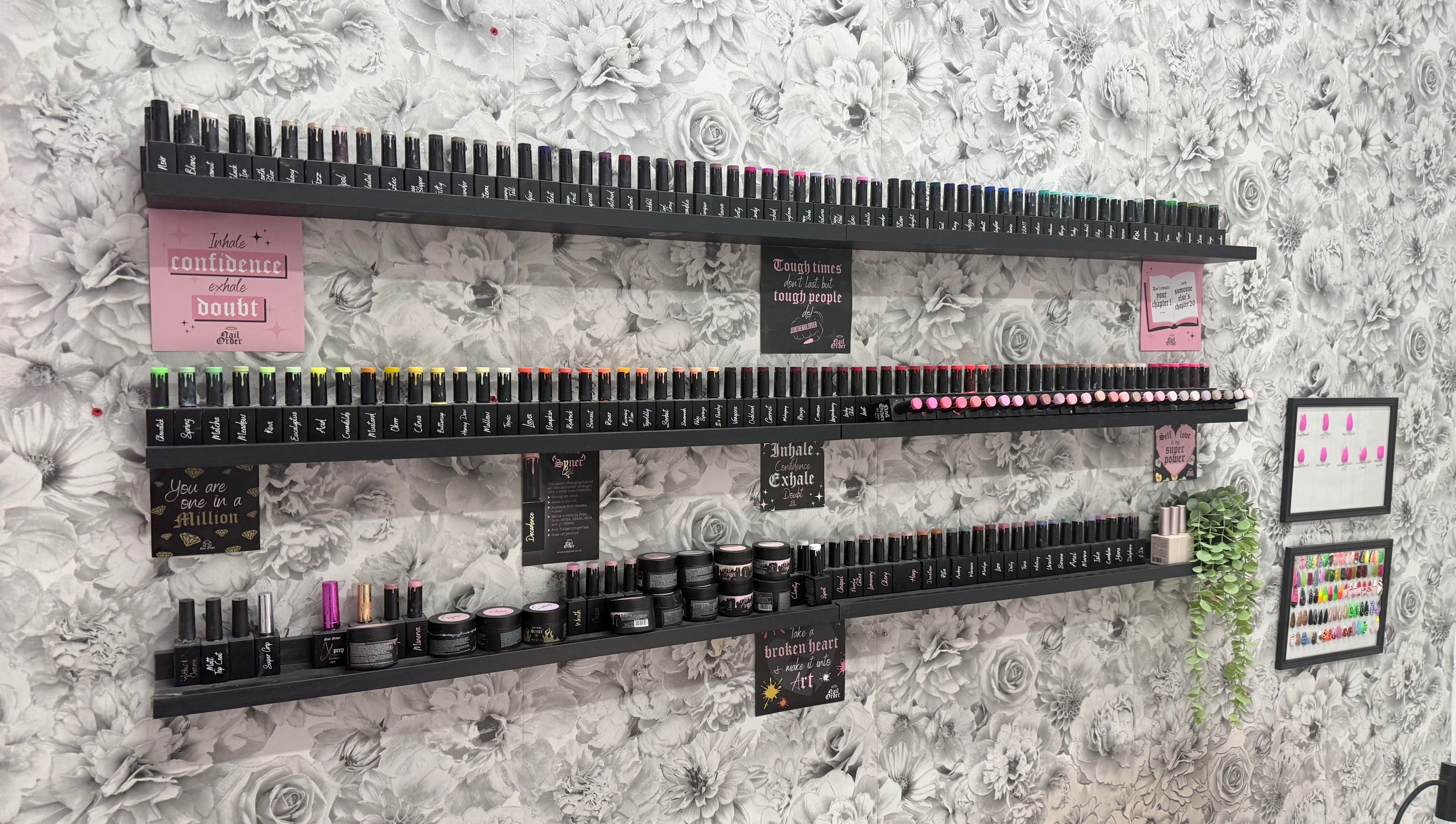 Nail polishes neatly arranged on black shelves at Nails by Emma in Norton, England, GB with floral background.