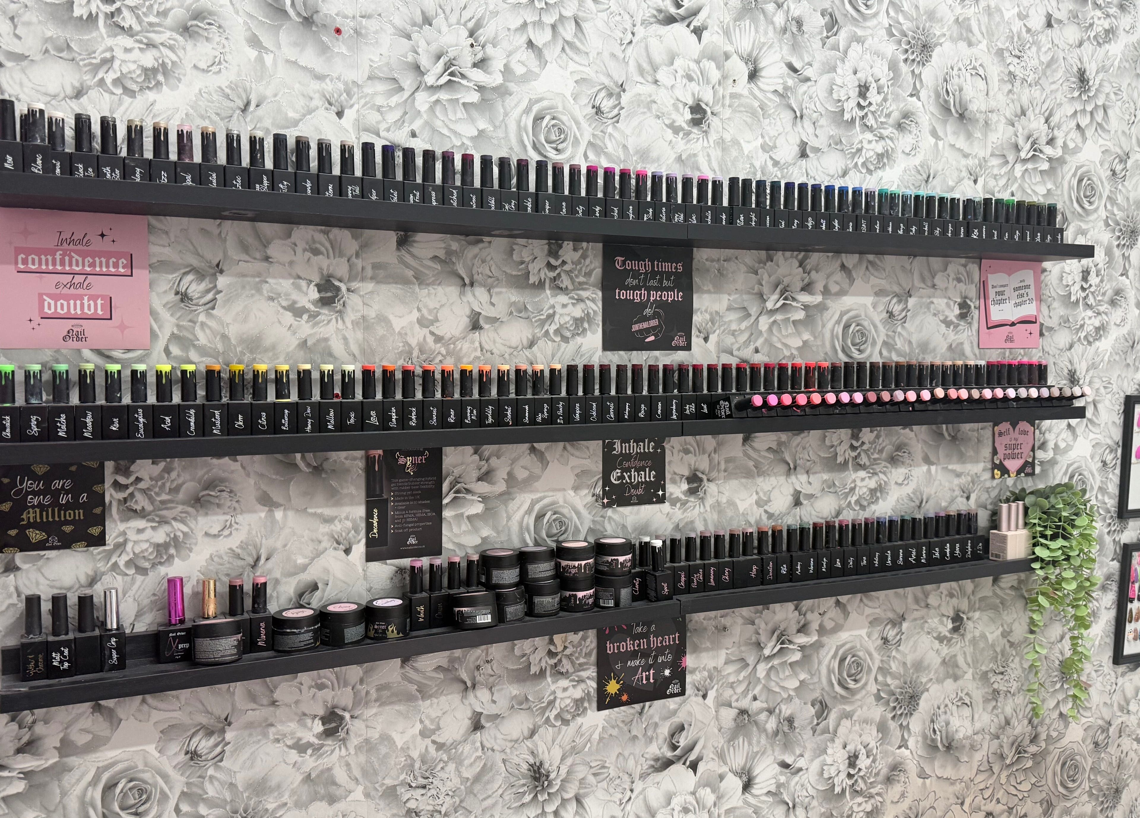 Nail polishes neatly arranged on black shelves at Nails by Emma in Norton, England, GB with floral background.
