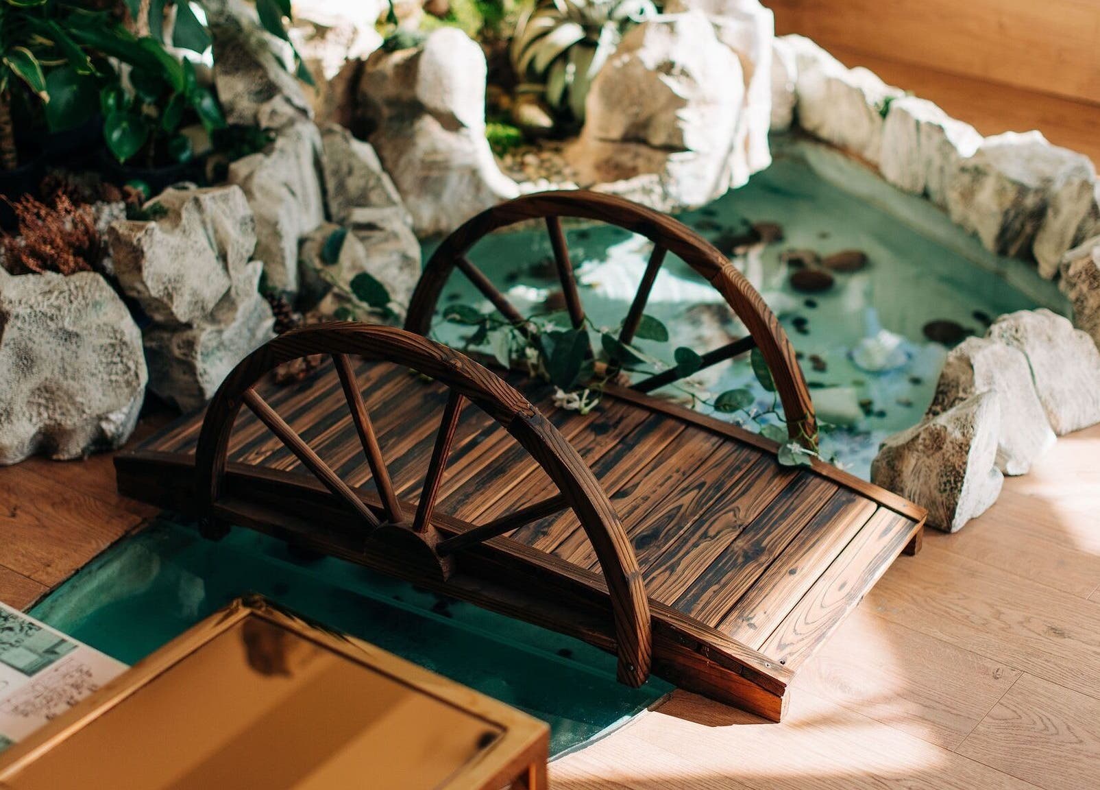 Tranquil wooden bridge over water at Bayou Spa, London, England, GB. Natural rocks and plants surround the area.
