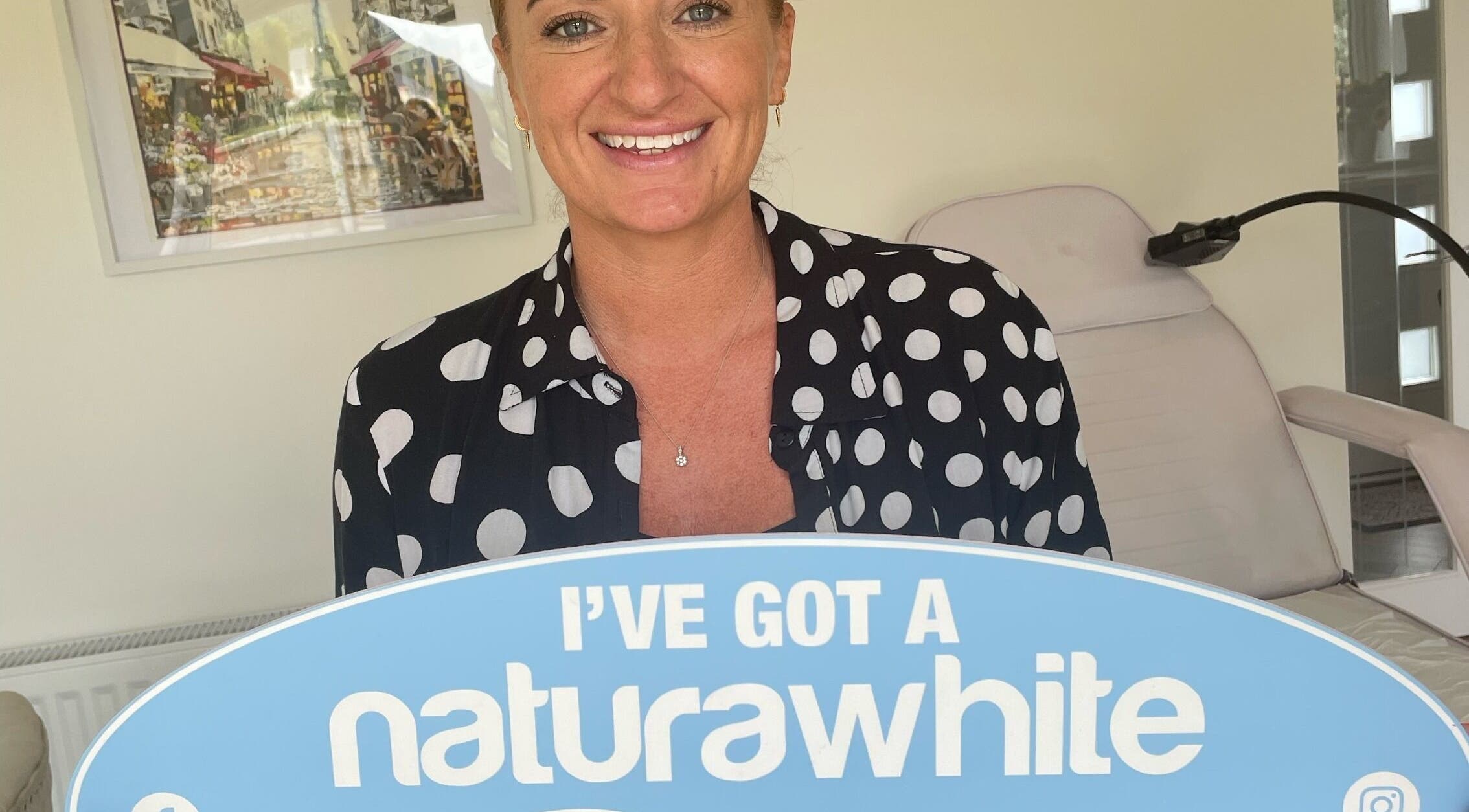 Smiling woman holding a 'naturawhite' sign at B-Radiant in Glynneath, Wales, GB.
