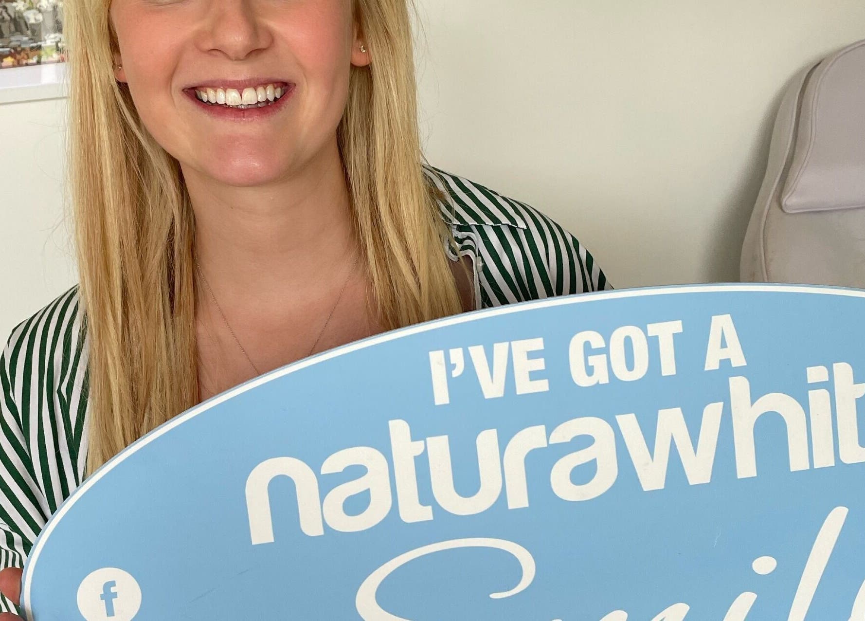 Smiling woman holding sign at B-Radiant, Glynneath, Wales, GB promoting NaturaWhite teeth whitening.