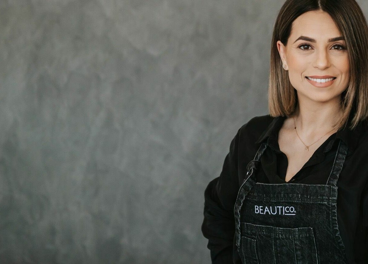A smiling stylist at BEAUTICO, Melbourne, Victoria, AU in a branded apron ready to assist clients.