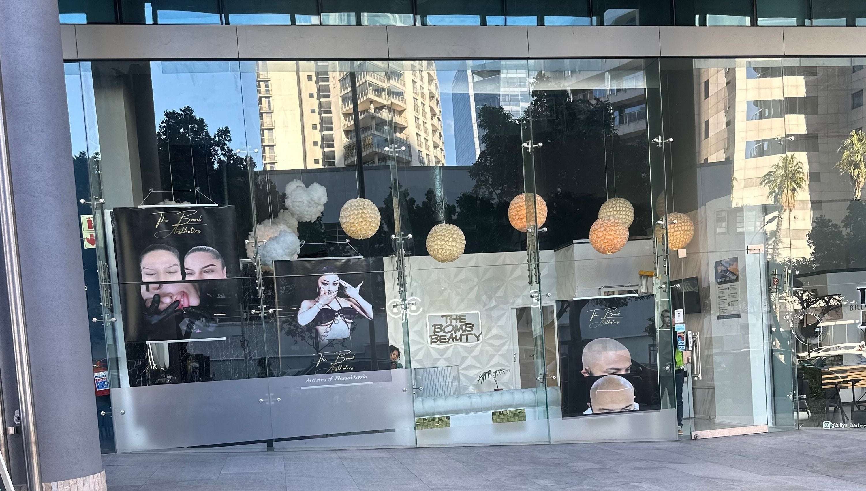 Glass facade of The bomb aesthetics Capetown, located in Cape Town, Western Cape, ZA, featuring large posters.