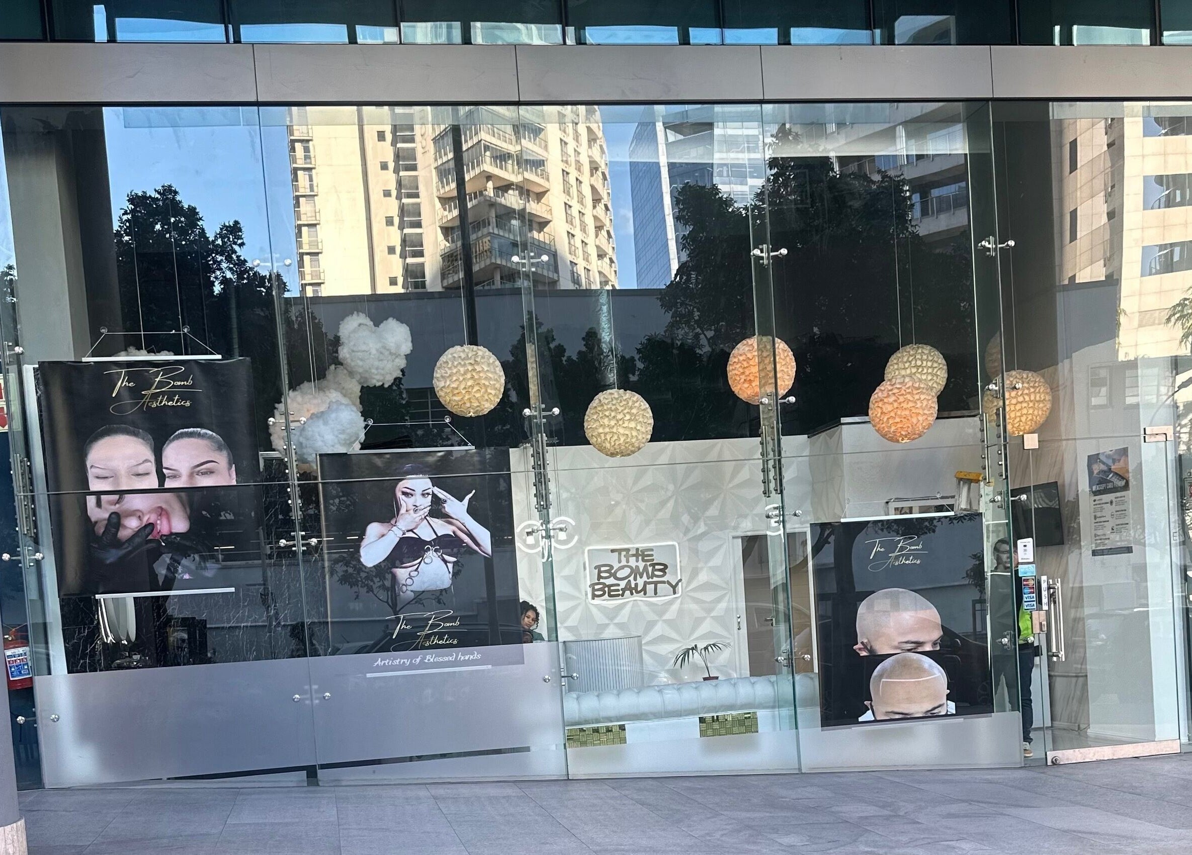 Glass facade of The bomb aesthetics Capetown, located in Cape Town, Western Cape, ZA, featuring large posters.