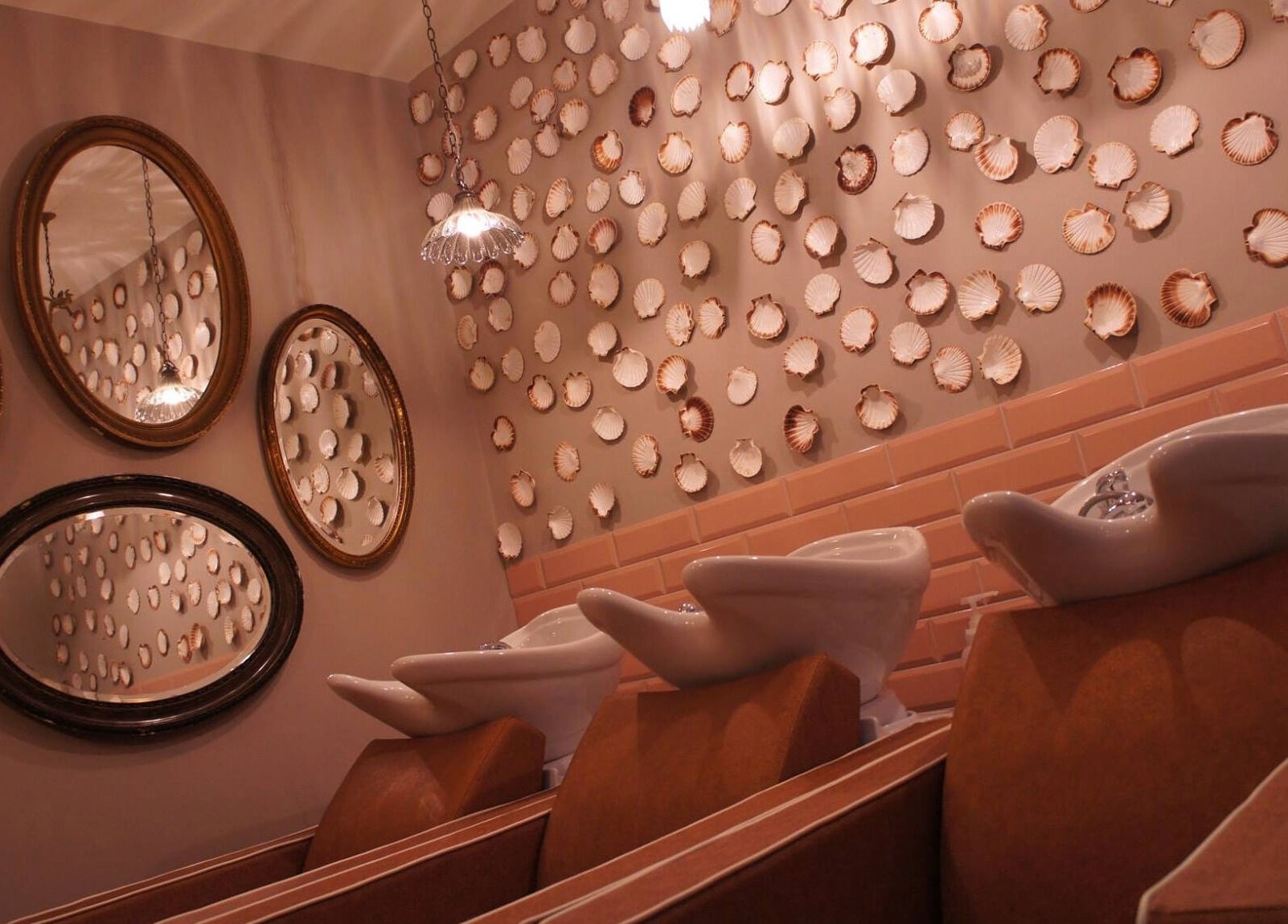 Elegant salon wash stations at The Curious Comb, London, England, GB, with decorative shell wall and mirrors.