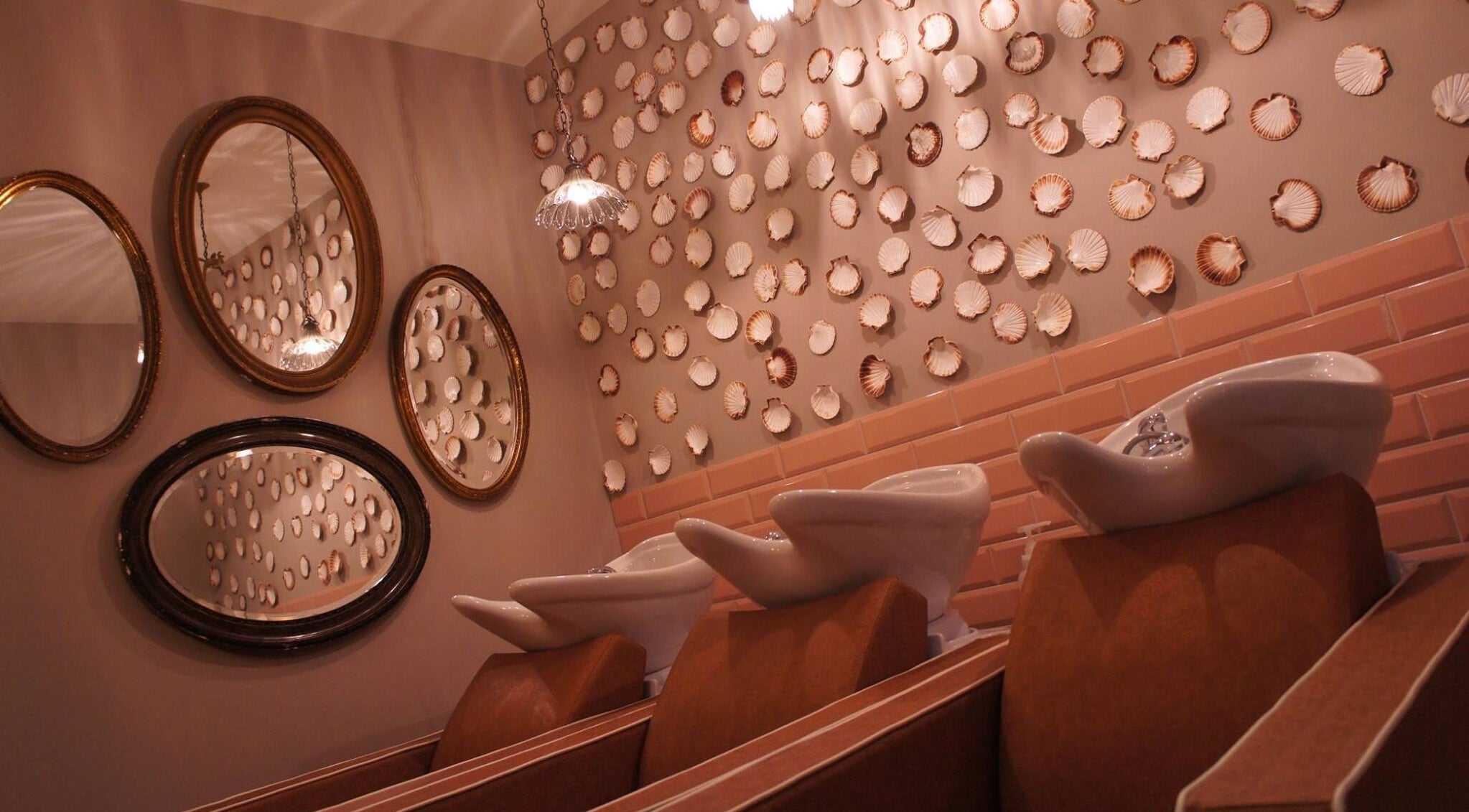 Elegant salon wash stations at The Curious Comb, London, England, GB, with decorative shell wall and mirrors.
