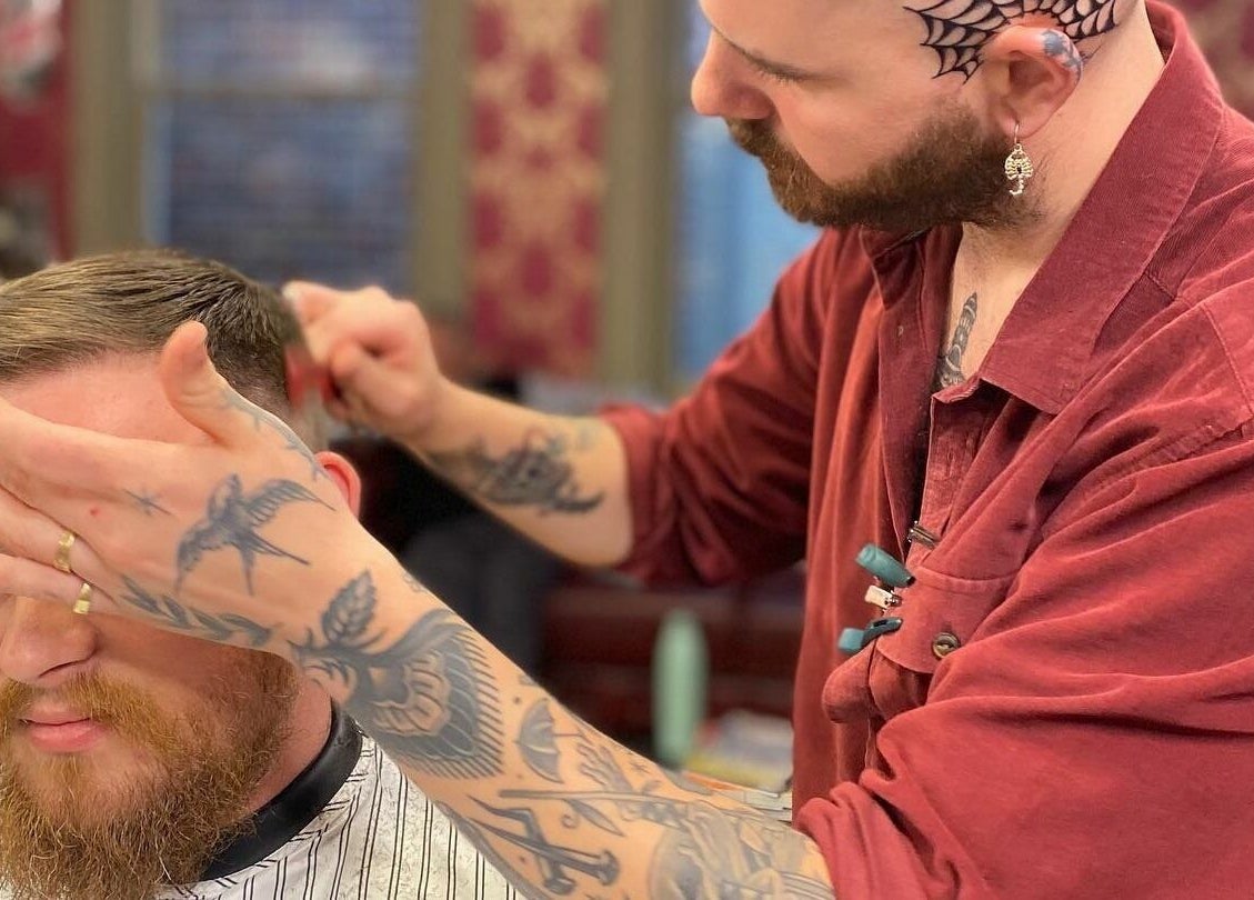 Tattooed barber expertly cutting hair at The Kingsway Barbershop in Launceston, Tasmania, AU.