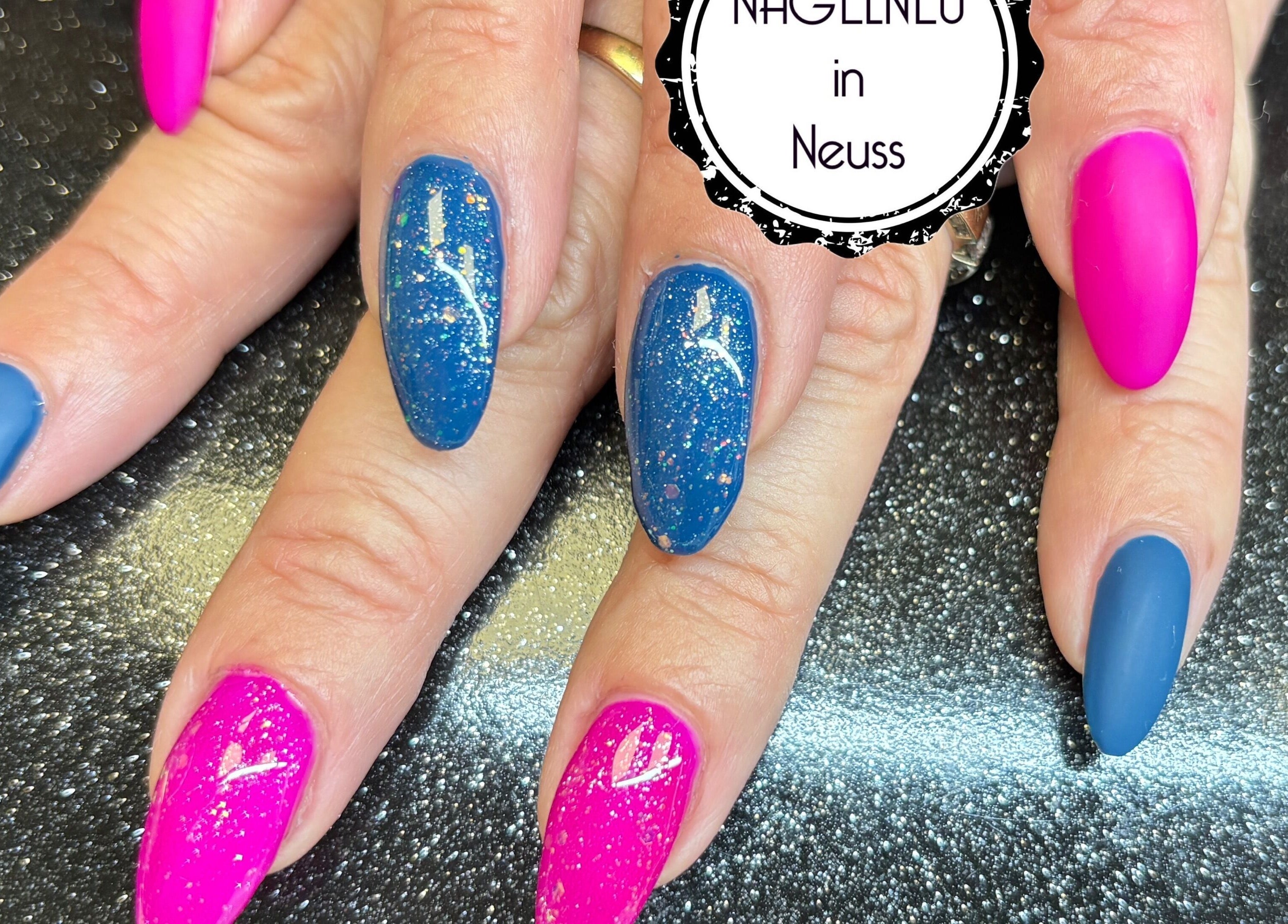Glitzernde Maniküre bei Nagelneu in Neuss, Nordrhein-westfalen, DE mit pinken und blauen Nägeln.