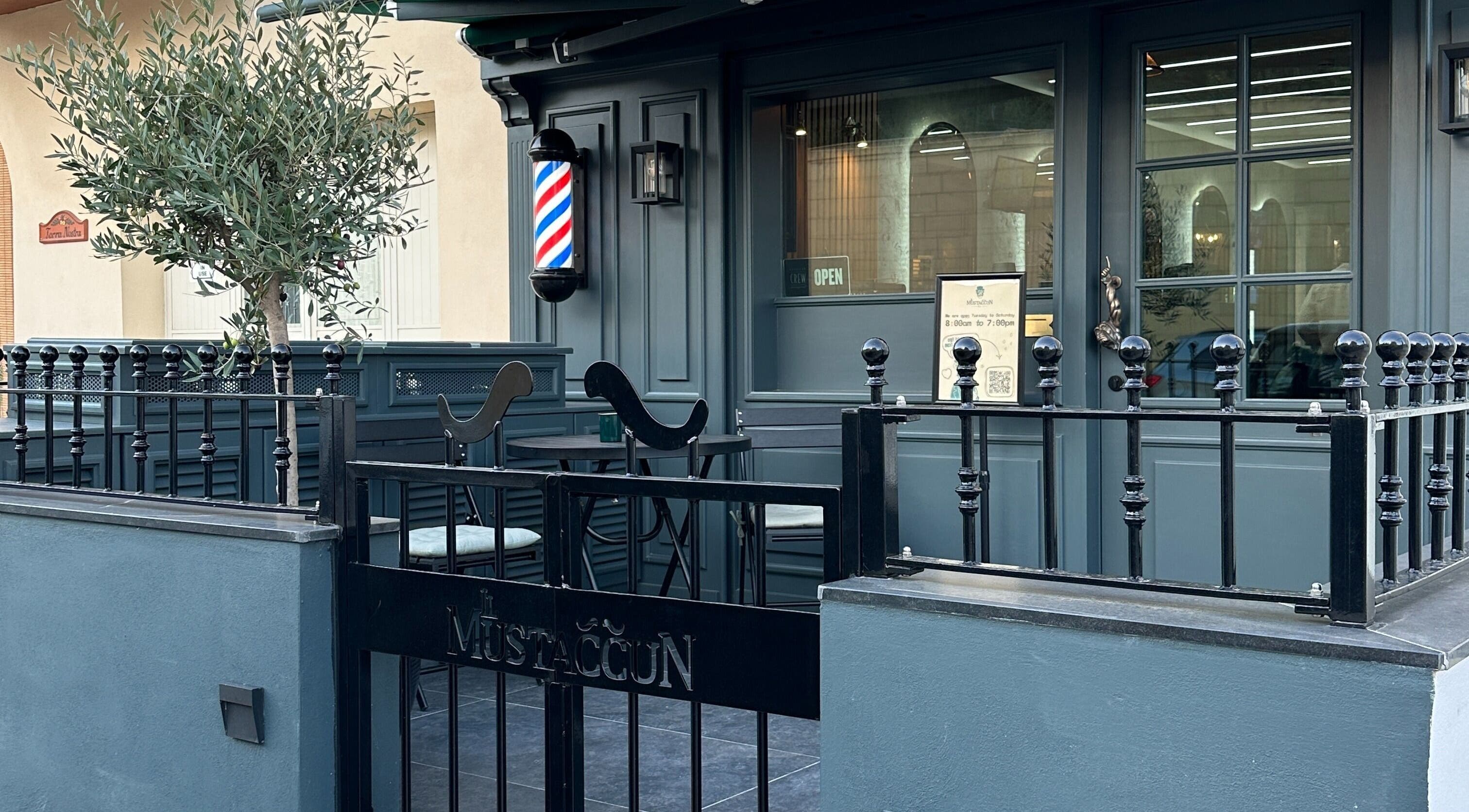 Entrance of il-Mustaċċun Barber in Ħal Lija, MT featuring sleek outdoor seating and vibrant barber pole.