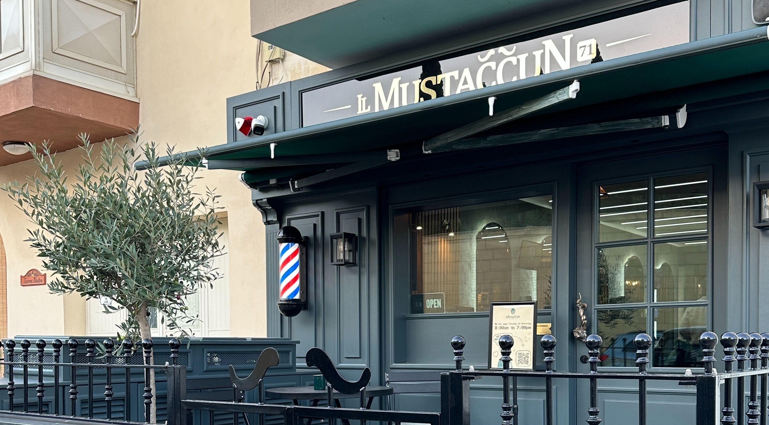 Exterior view of il-Mustaċċun Barber in Ħal Lija, MT with stylish black decor and barber pole.