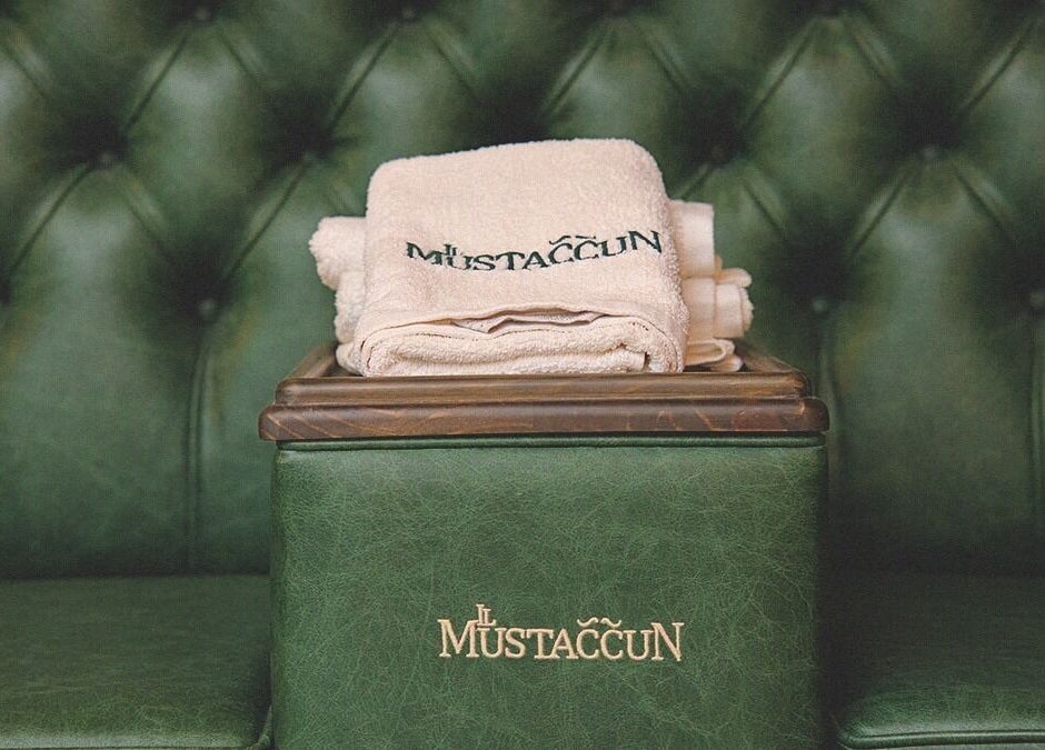 Luxurious towels with il-Mustaċċun Barber logo on green tufted seating in Ħal Lija, MT.