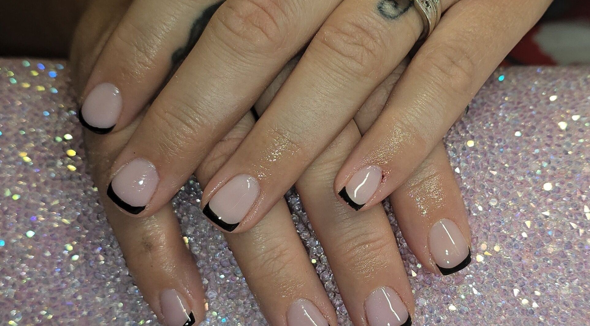 Elegant black French tips manicure at Nailed It By Laura, Carluke, Scotland, GB on sparkling surface.
