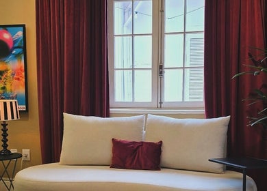 Sala de espera aconchegante no Tom Maia Hair Studio em Rio Grande Do Sul, Brasil, com sofá creme e cortinas vermelhas.