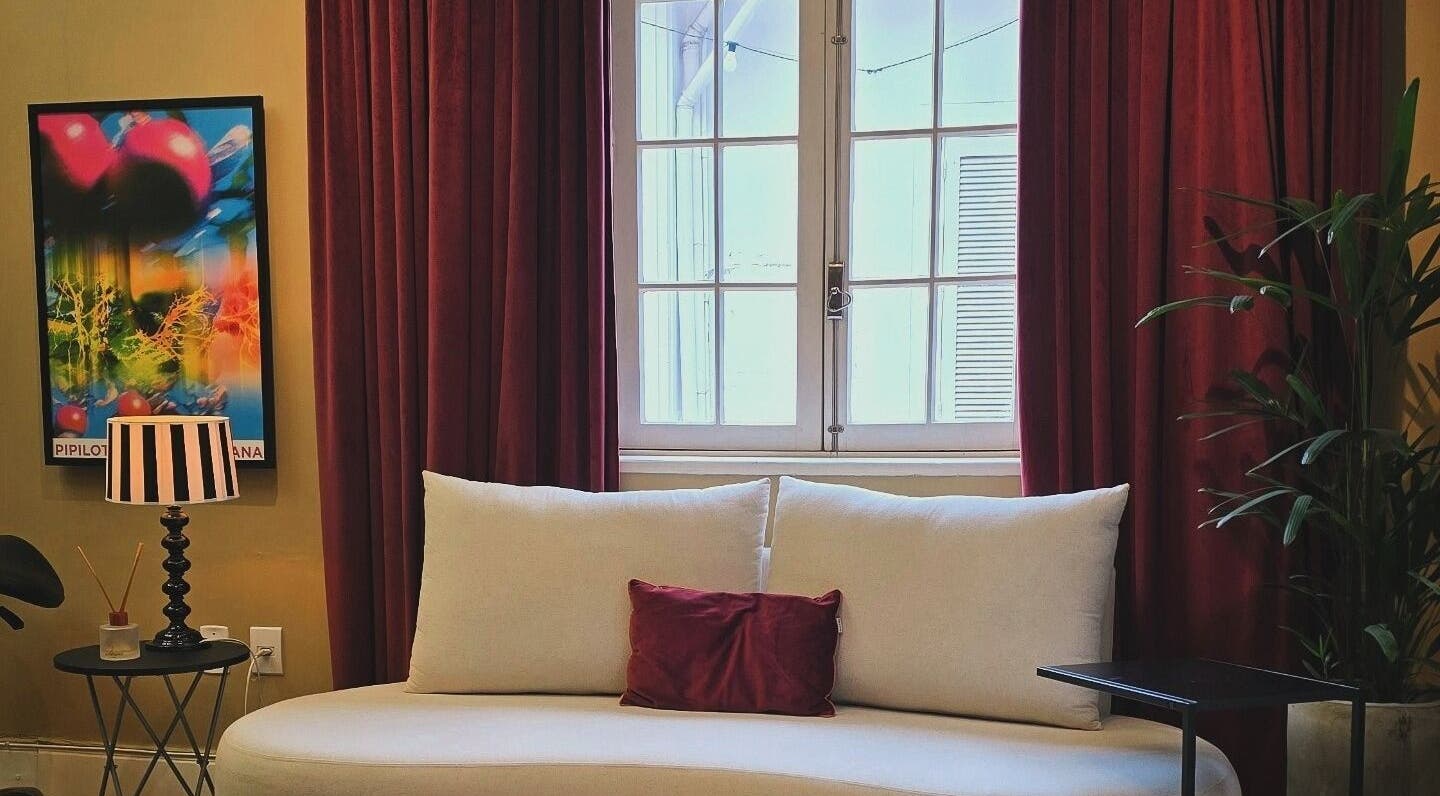 Sala de espera aconchegante no Tom Maia Hair Studio em Rio Grande Do Sul, Brasil, com sofá creme e cortinas vermelhas.