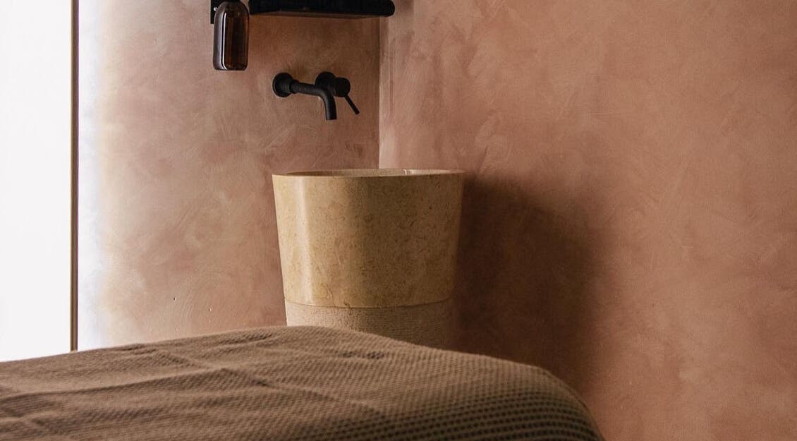 A calming, beige-toned spa room at MASAJ Marylebone, London, England, GB, featuring a sleek stone basin.