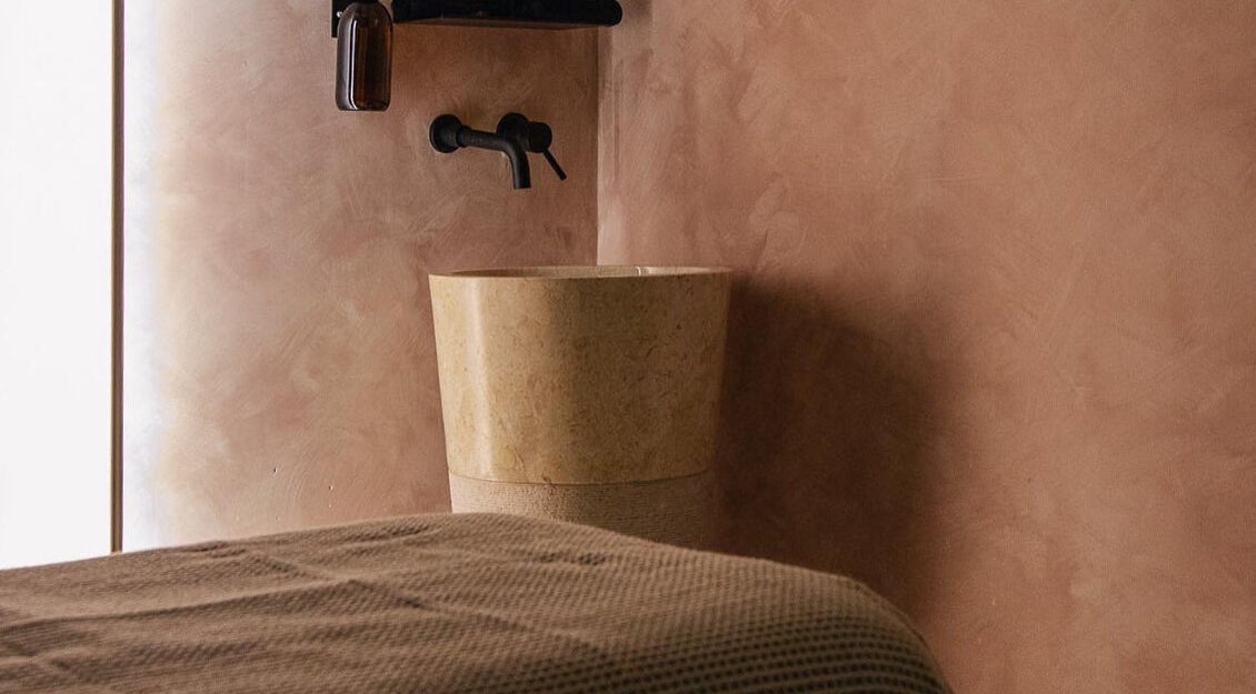 A calming, beige-toned spa room at MASAJ Marylebone, London, England, GB, featuring a sleek stone basin.