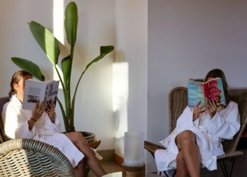 Guests enjoying books at Wave Nordic Spa, Mount Elgin, Ontario, CA, in relaxed wicker chairs by a cozy fire.