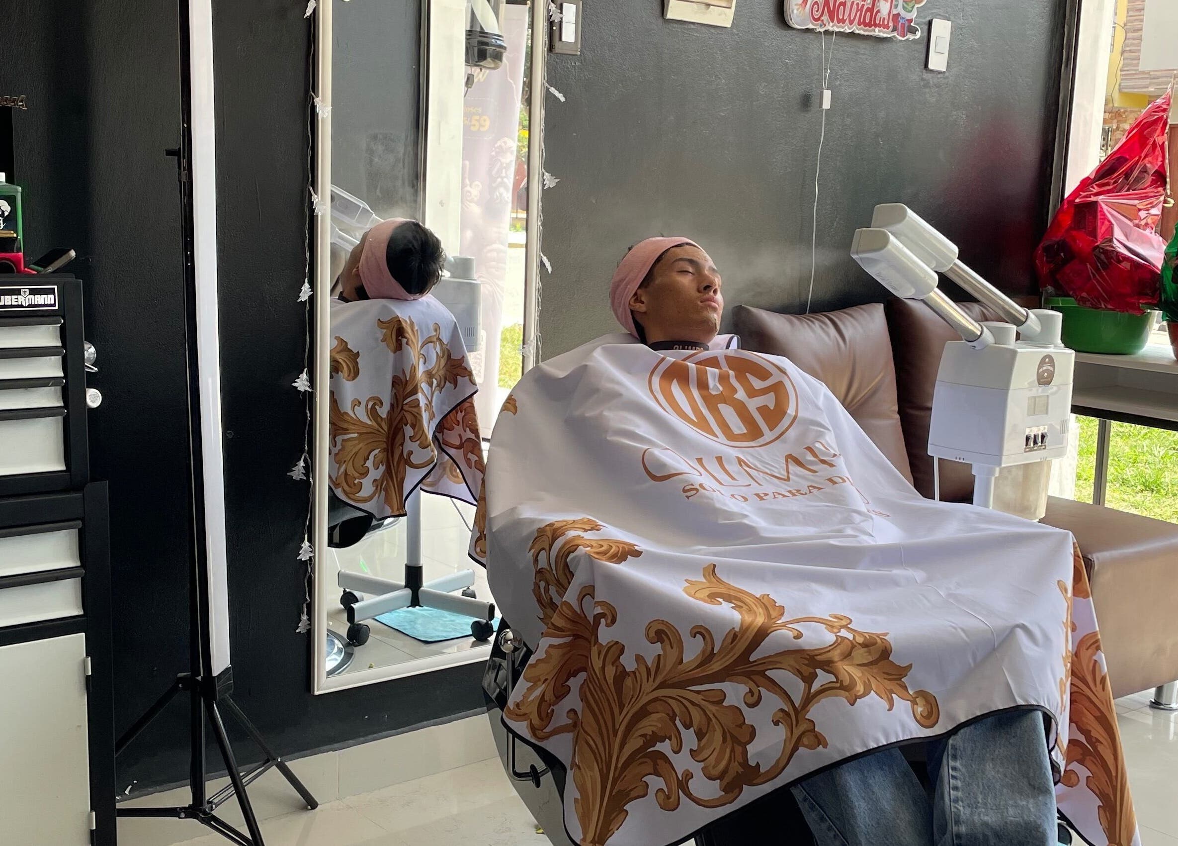 Cliente relajándose en Olimpo barber studio, Chimbote, Áncash, PE, con una capa ornamental.