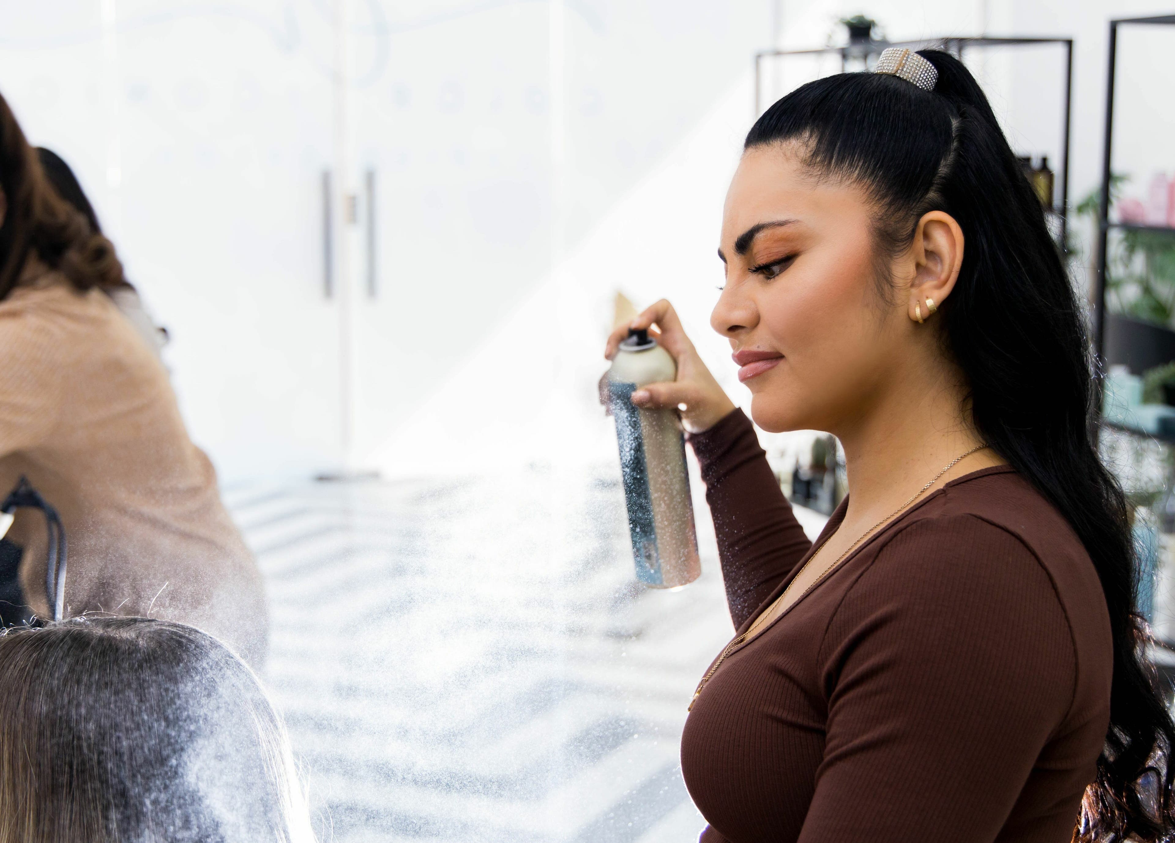 Stylist at Color Iconic Ladies Salon in Dubai, AE, applying hairspray for a polished look.