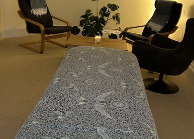 Relaxing massage room at Christie Louise Massage in Cirencester, England, GB with patterned table cover and cozy chairs.