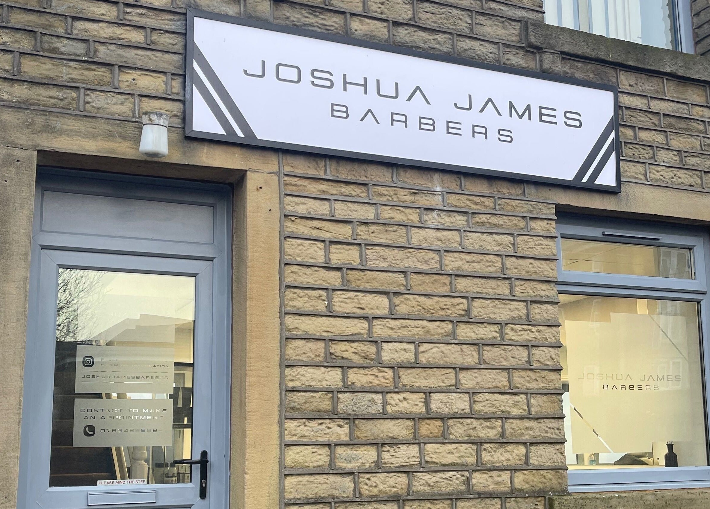 Entrance of Joshua James Barbers in Huddersfield, England, GB with modern signage on brick exterior.