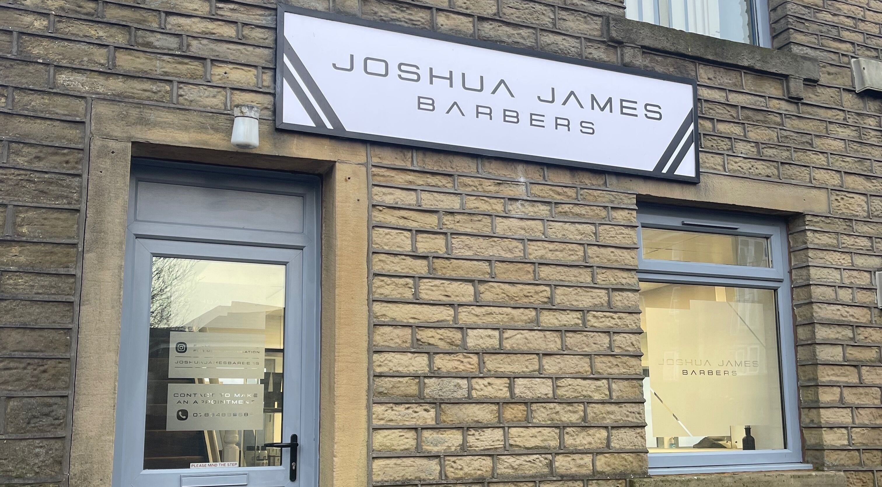 Entrance of Joshua James Barbers in Huddersfield, England, GB with modern signage on brick exterior.