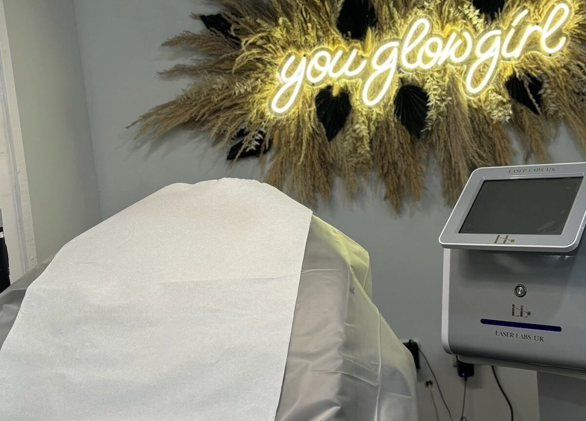 Treatment room with aesthetic machine at House of Boo, Petersfield, England, GB under glowing 'you glow girl' sign.