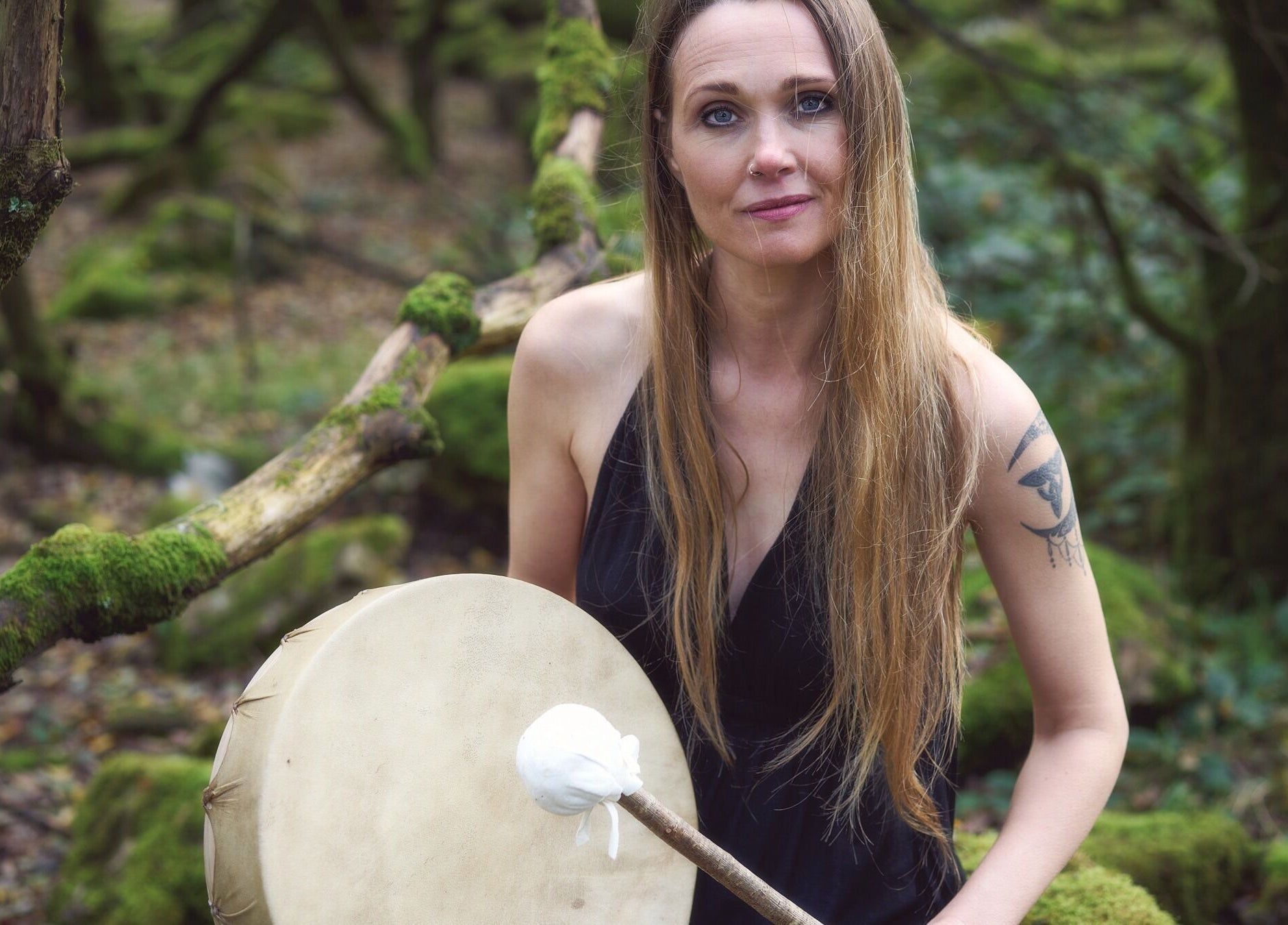 Woman with drum in woodland at Kernow Serenity, Truro, England, GB, offering a tranquil wellness retreat.