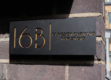 Sign for Glaysson Carvalho Hair Studio at 16B, London, England, GB, on a brick wall.