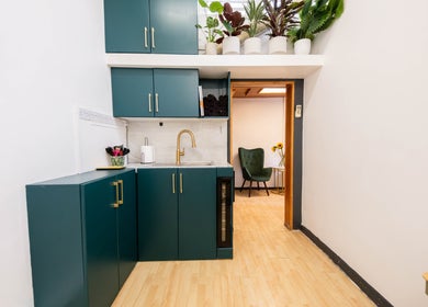Modern kitchenette in Glaysson Carvalho Hair Studio, London, England, GB, featuring teal cabinets and potted plants.