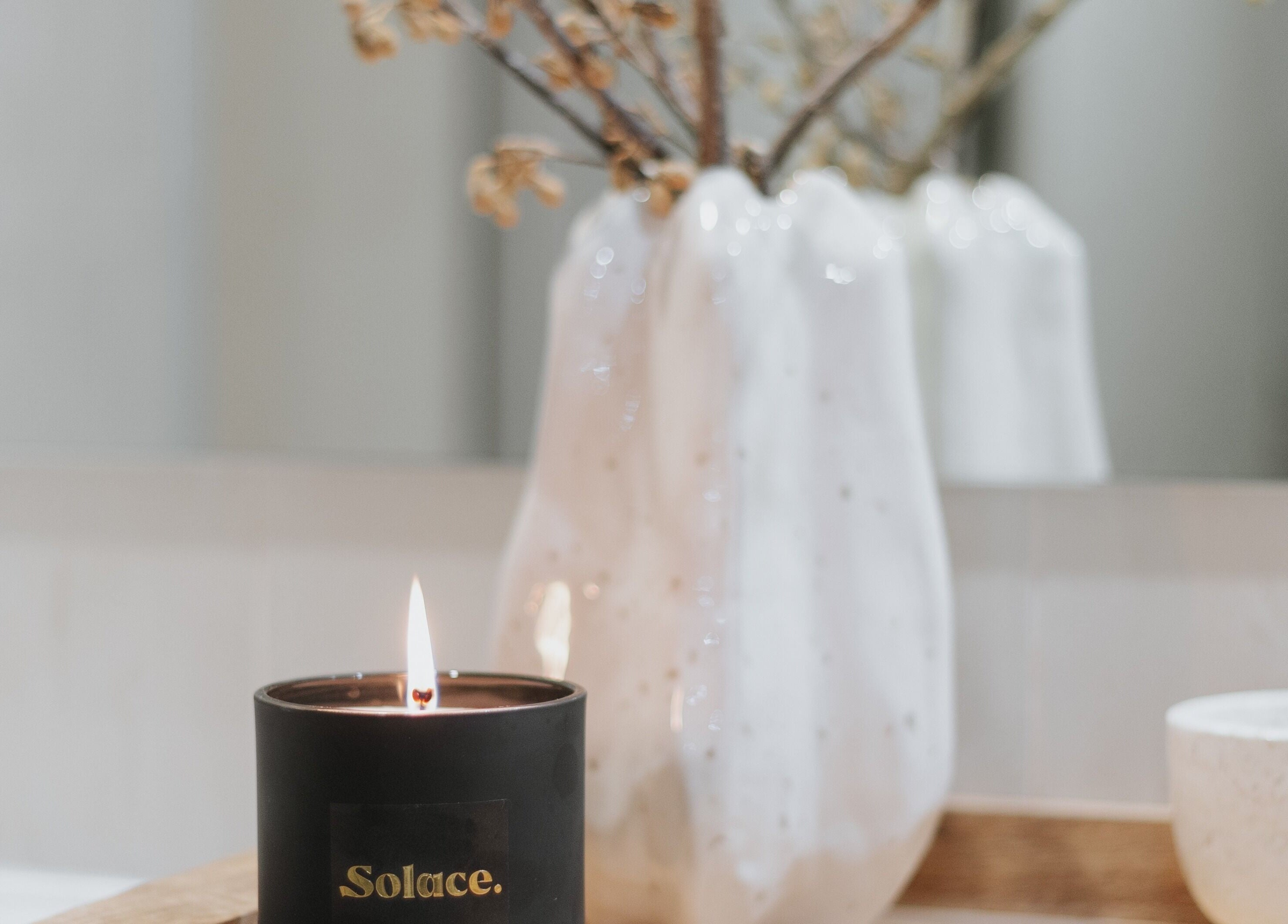 Lit Solace Day Spa candle near vase at Scarborough, Western Australia, AU for a tranquil ambiance.