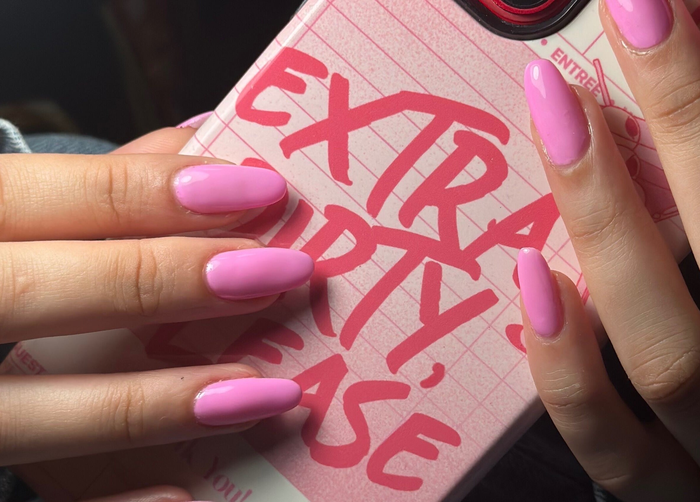 Vibrant pink manicured nails by Nails by Kelly in Hollywood, Florida, US, held over a stylish phone case.