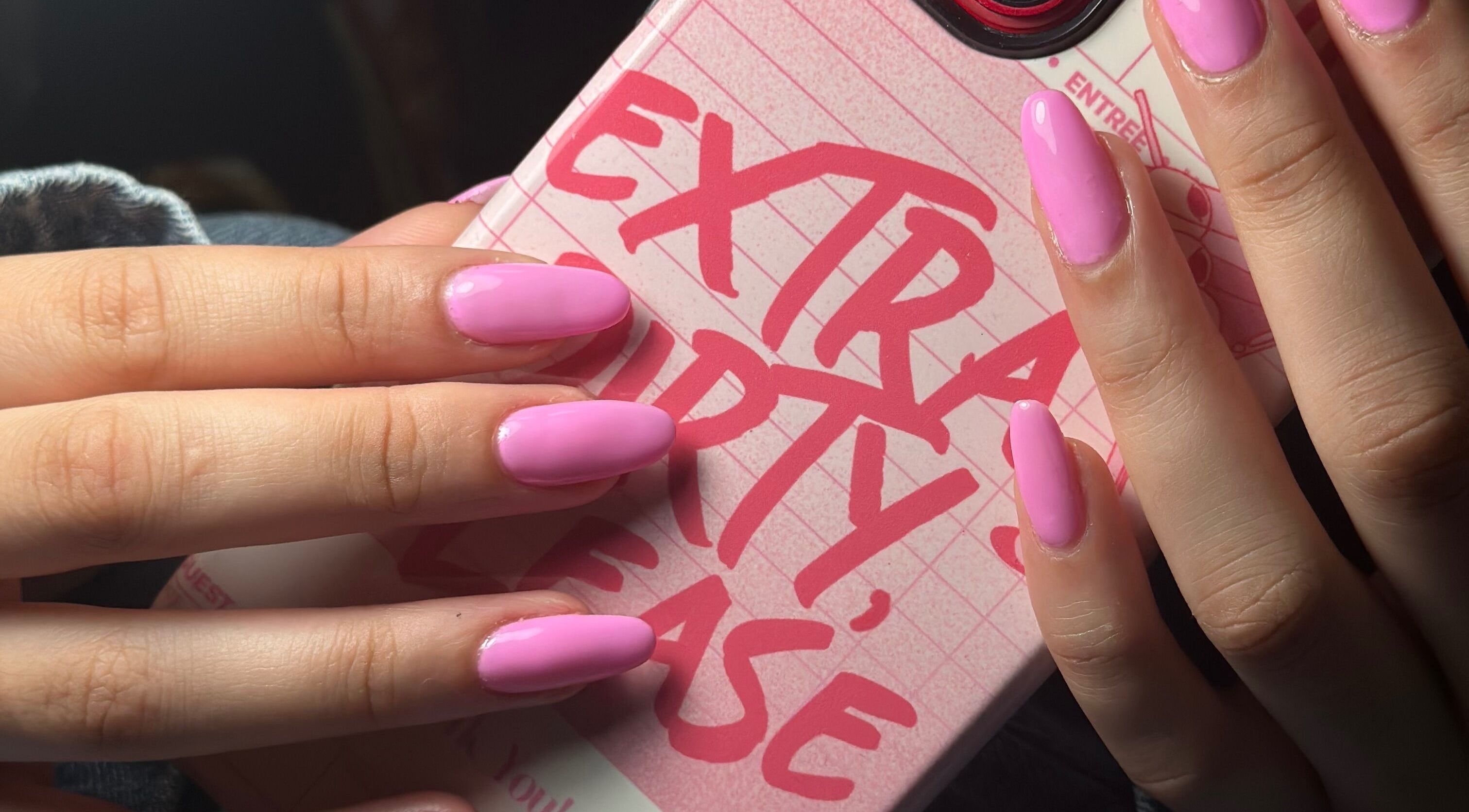 Vibrant pink manicured nails by Nails by Kelly in Hollywood, Florida, US, held over a stylish phone case.
